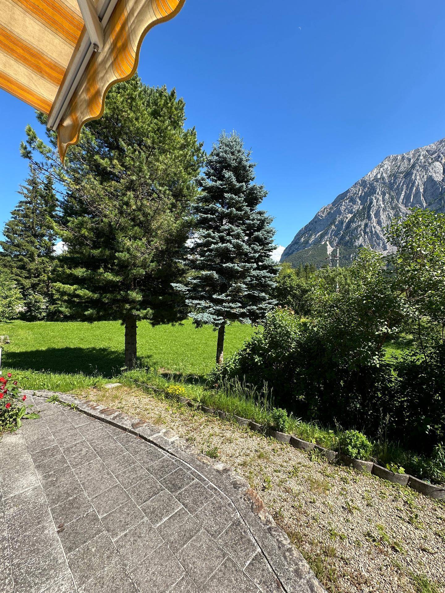 Gepflasterte Terrasse mit Blick auf die umliegende Berglandschaft und grüne Bäume.