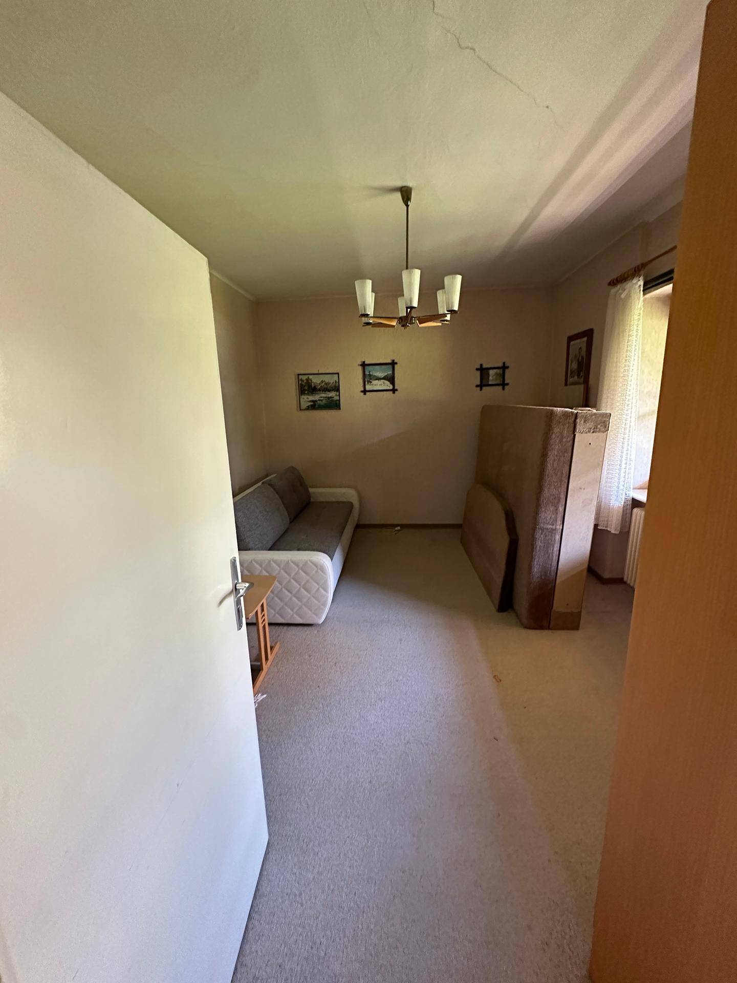 Schlafzimmer mit Teppichboden und Sofa, derzeit als Gästezimmer oder Abstellraum genutzt.