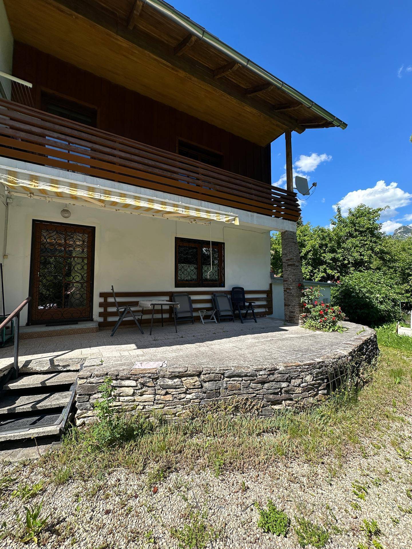 Große gepflasterte Terrasse mit Steinmauer und Markise, ideal für Mahlzeiten im Freien.