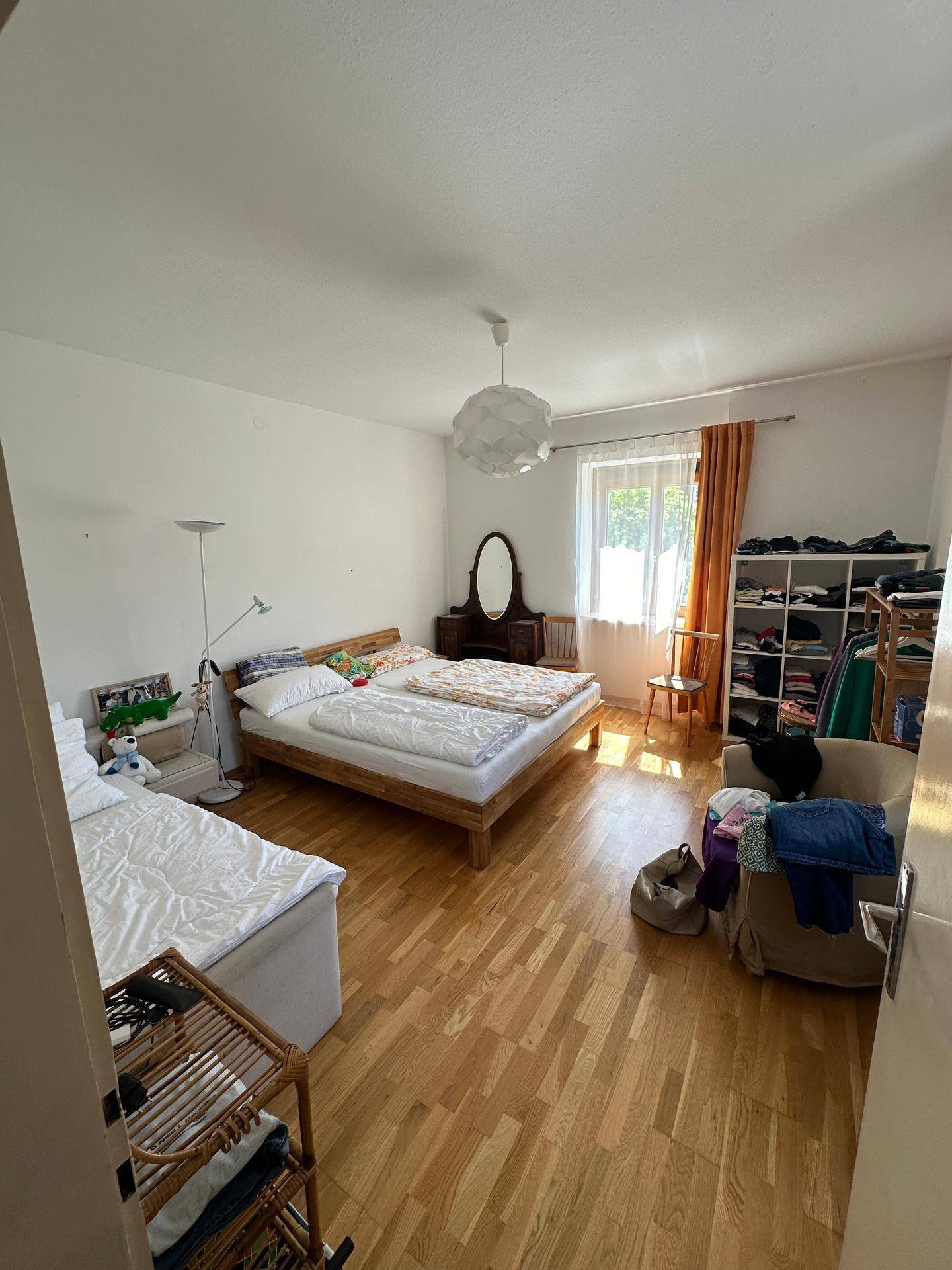 Helles Schlafzimmer mit Holzboden, zwei Betten und einfacher, funktionaler Einrichtung.