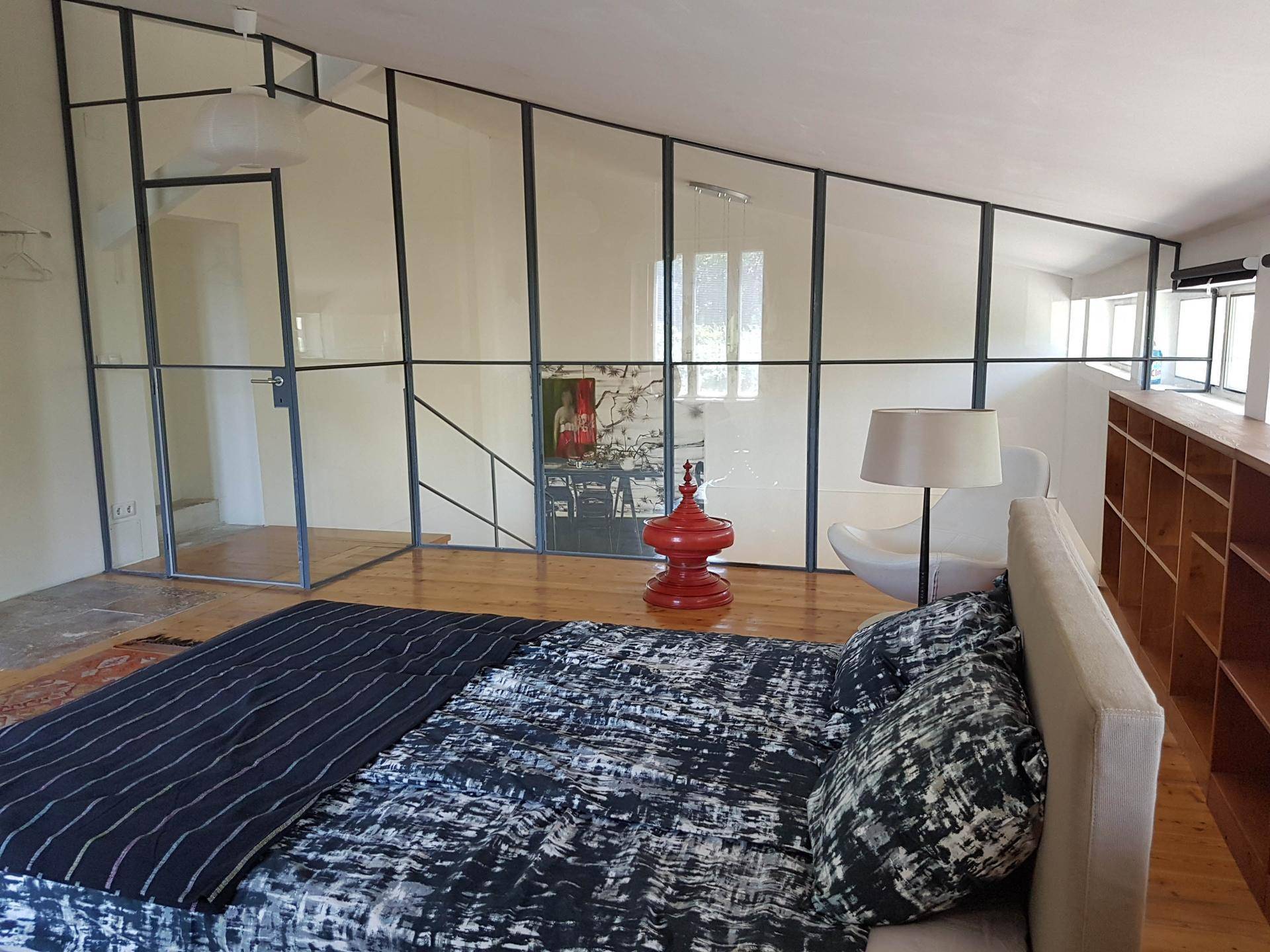 Modernes Schlafzimmer mit Holzboden, Glaswänden und integrierten Regalen, hell und offen gestaltet.