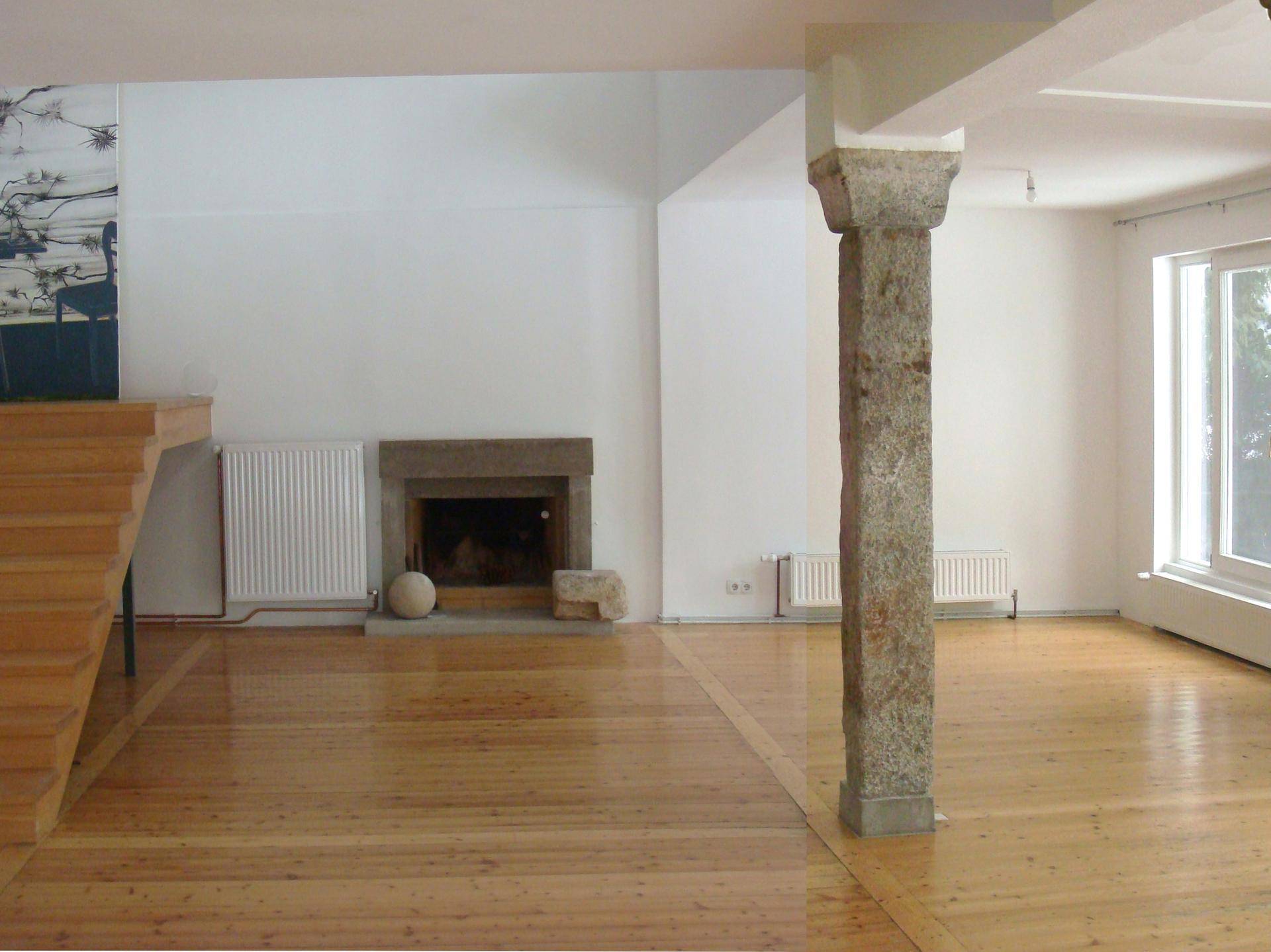 Heller Wohnbereich mit Holzboden, Steinkamin und offener Treppe, die zum oberen Stockwerk führt.