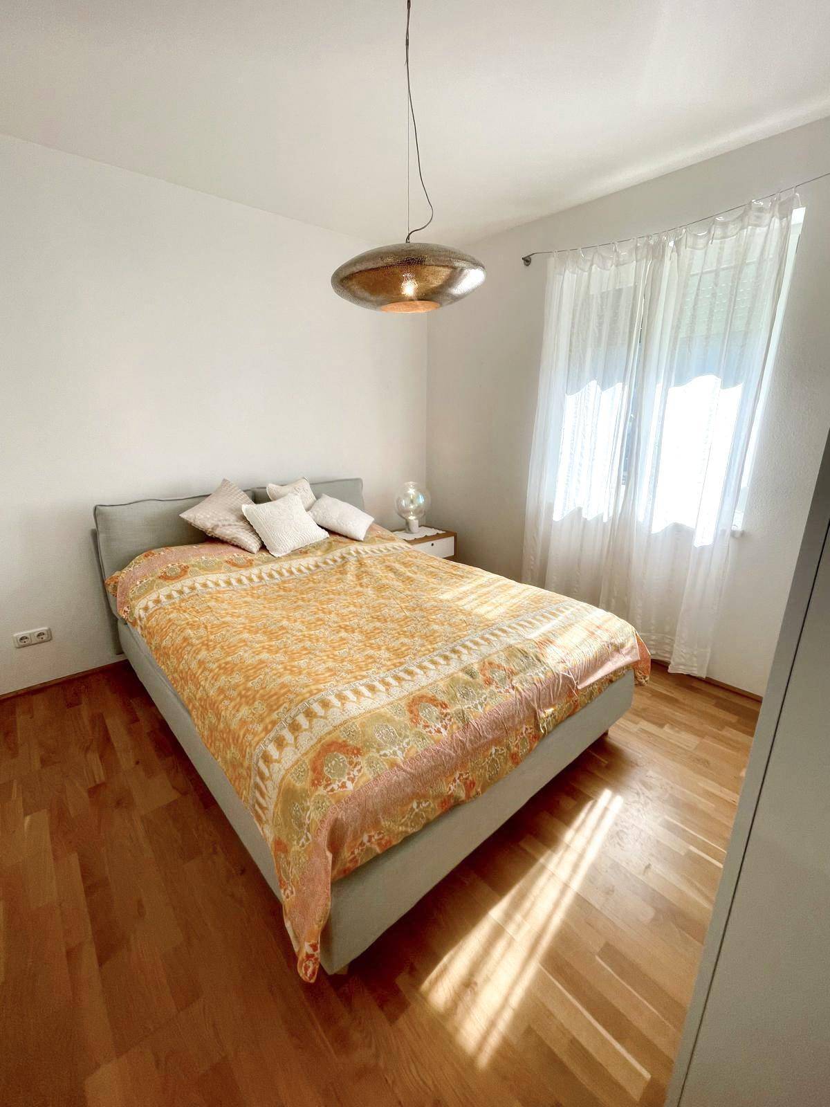 Gemütliches Schlafzimmer mit Doppelbett, Nachttisch und viel Tageslicht durch das Fenster.