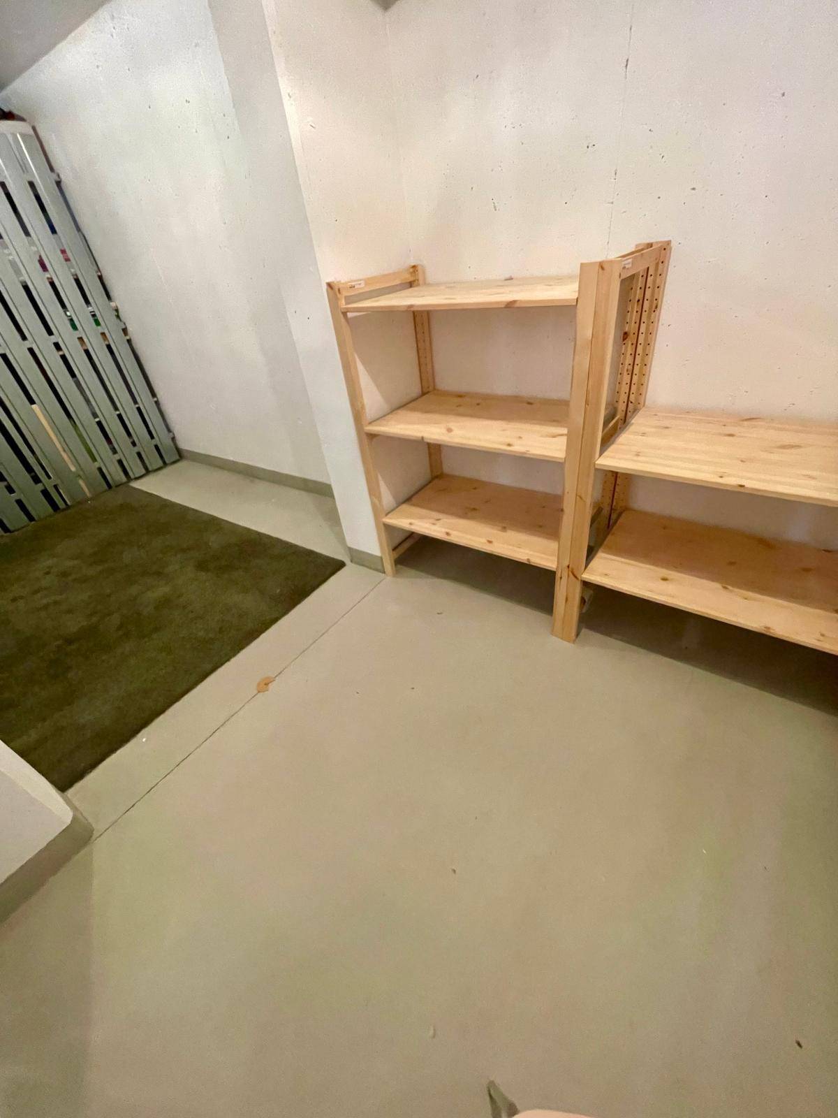Praktischer Abstellraum mit Holzregalen und einem Teppich auf dem Betonboden.