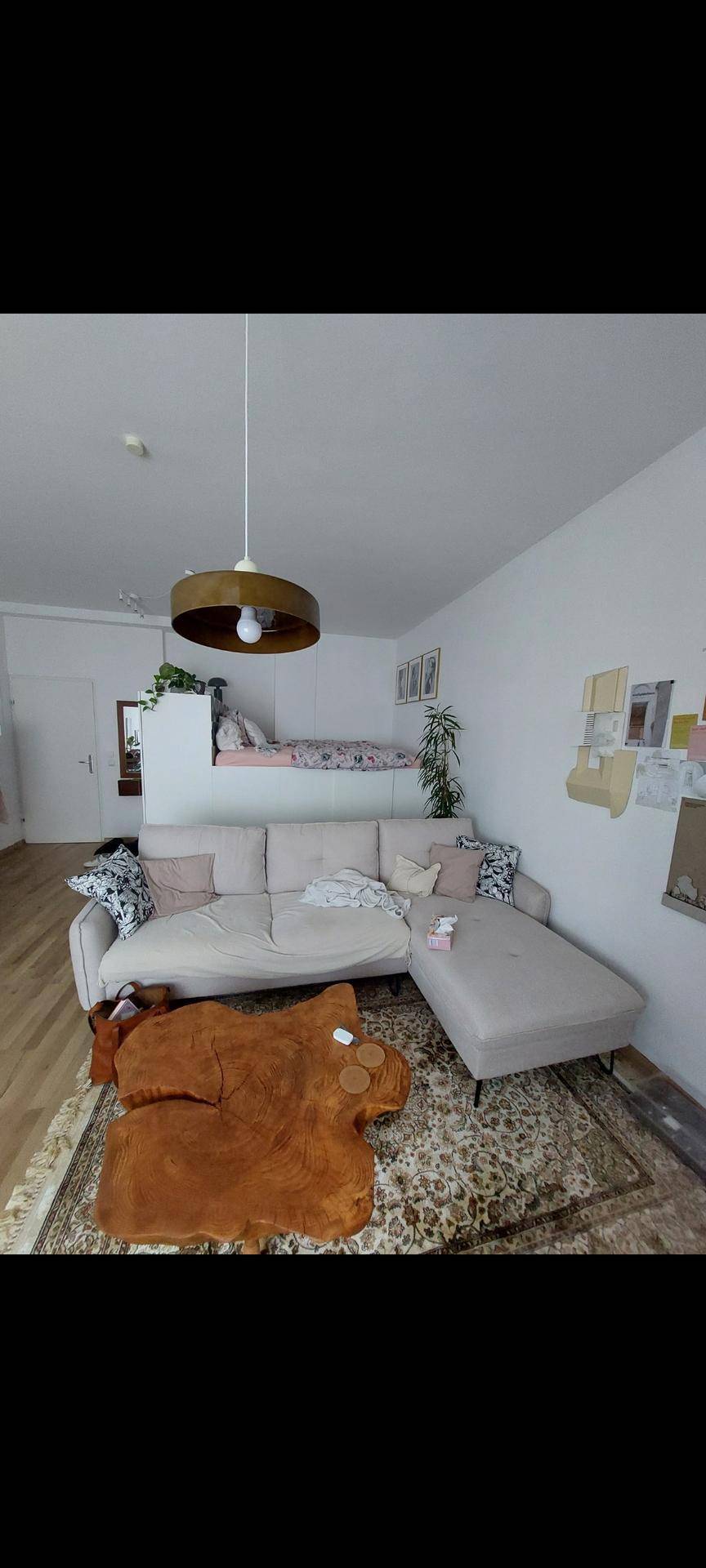 Gemütlicher Wohnbereich mit beigem Ecksofa, Teppich und integriertem Schlafbereich.