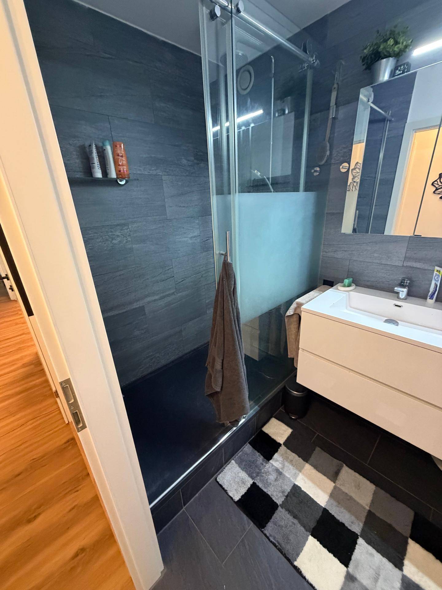 Modernes Badezimmer mit großer begehbarer Dusche, dunklen Fliesen und einem einzelnen Waschbecken.
