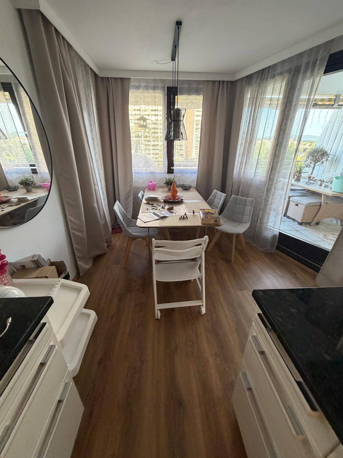 Heller Essbereich mit großem Tisch, Stühlen und Zugang zu einem Balkon durch breite Fenster.