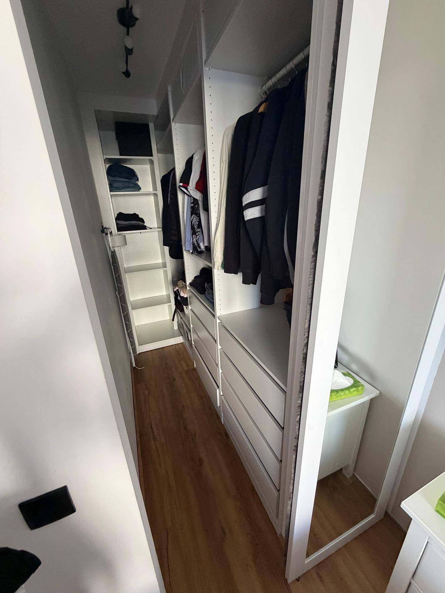 Langer begehbarer Kleiderschrank mit weißen Regalen und Schubladen für Kleidung und Aufbewahrung.