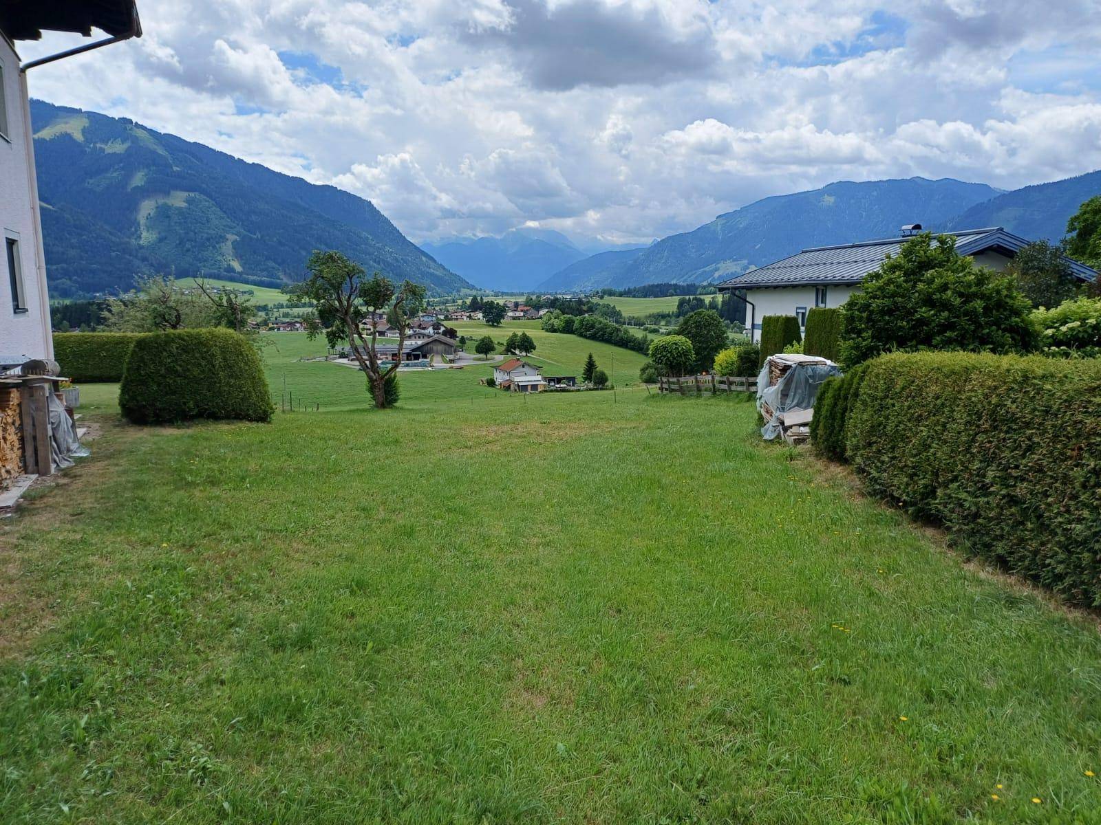 Idyllische Landschaft mit weiten Grünflächen, vereinzelten Häusern und einer malerischen Bergkette am Horizont.
