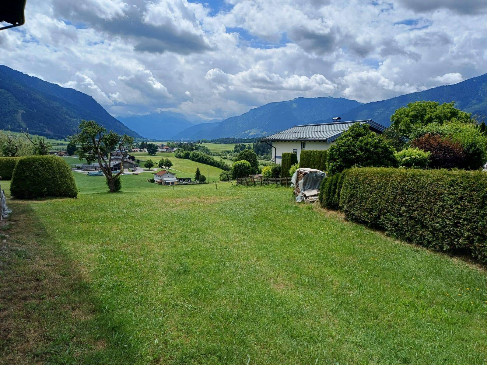 Weitläufige grüne Wiesen mit einem Haus und einer beeindruckenden Bergkulisse unter bewölktem Himmel.