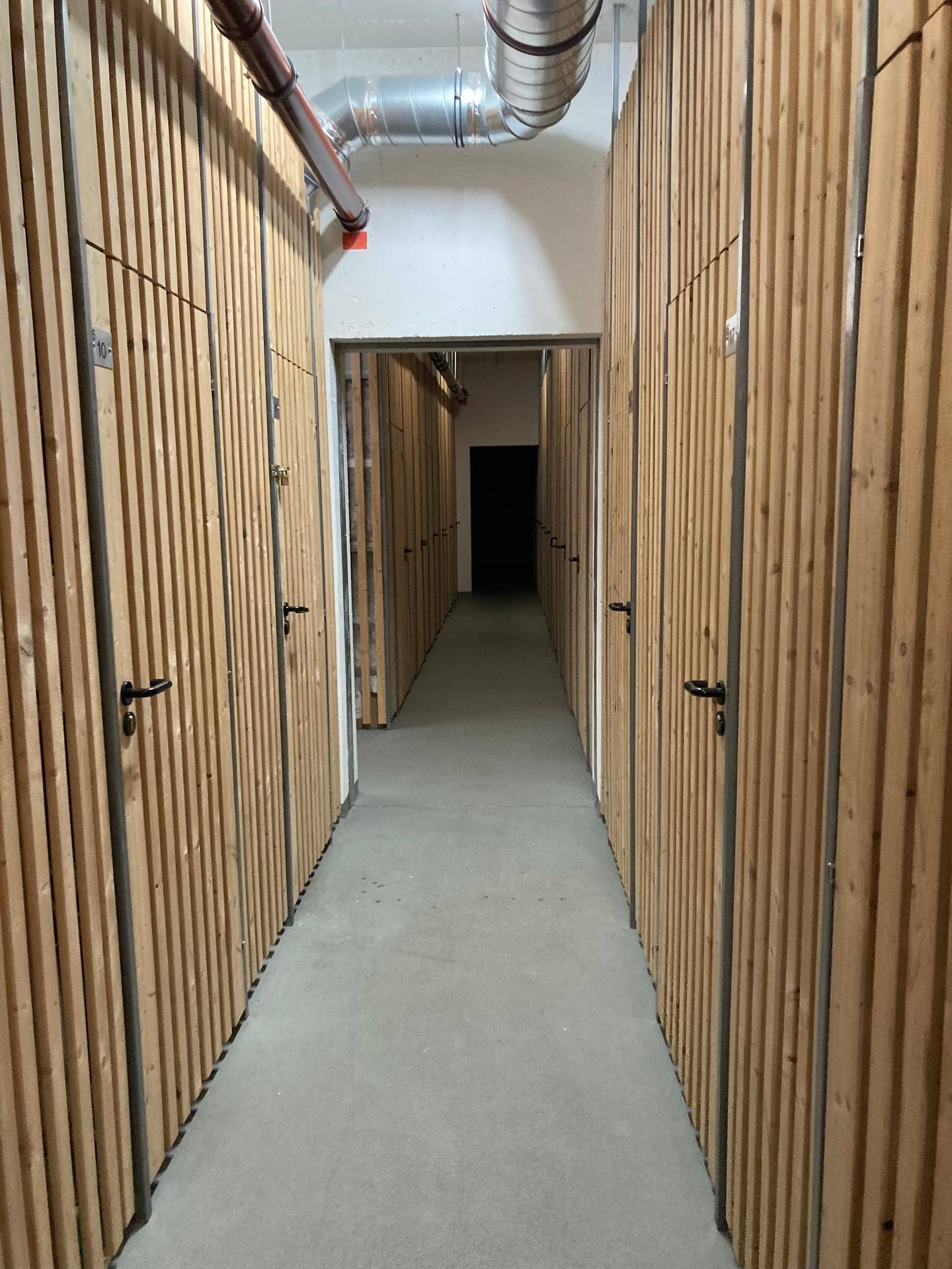 Langer Gang im Keller mit vielen Holzverschlägen für Abstellräume.