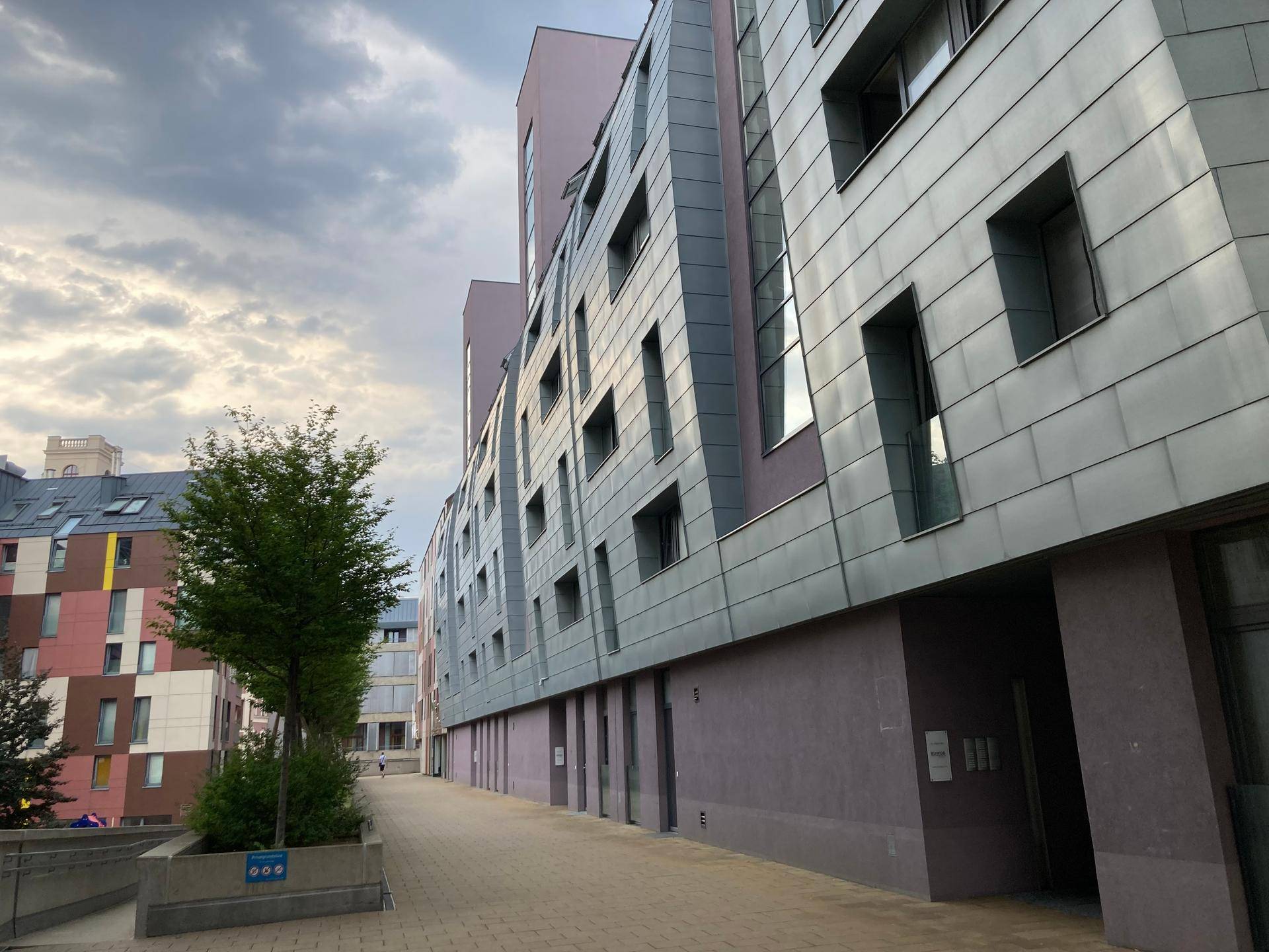 Moderne Gebäudefassade mit grauen Paneelen und großen Fenstern unter bewölktem Himmel.