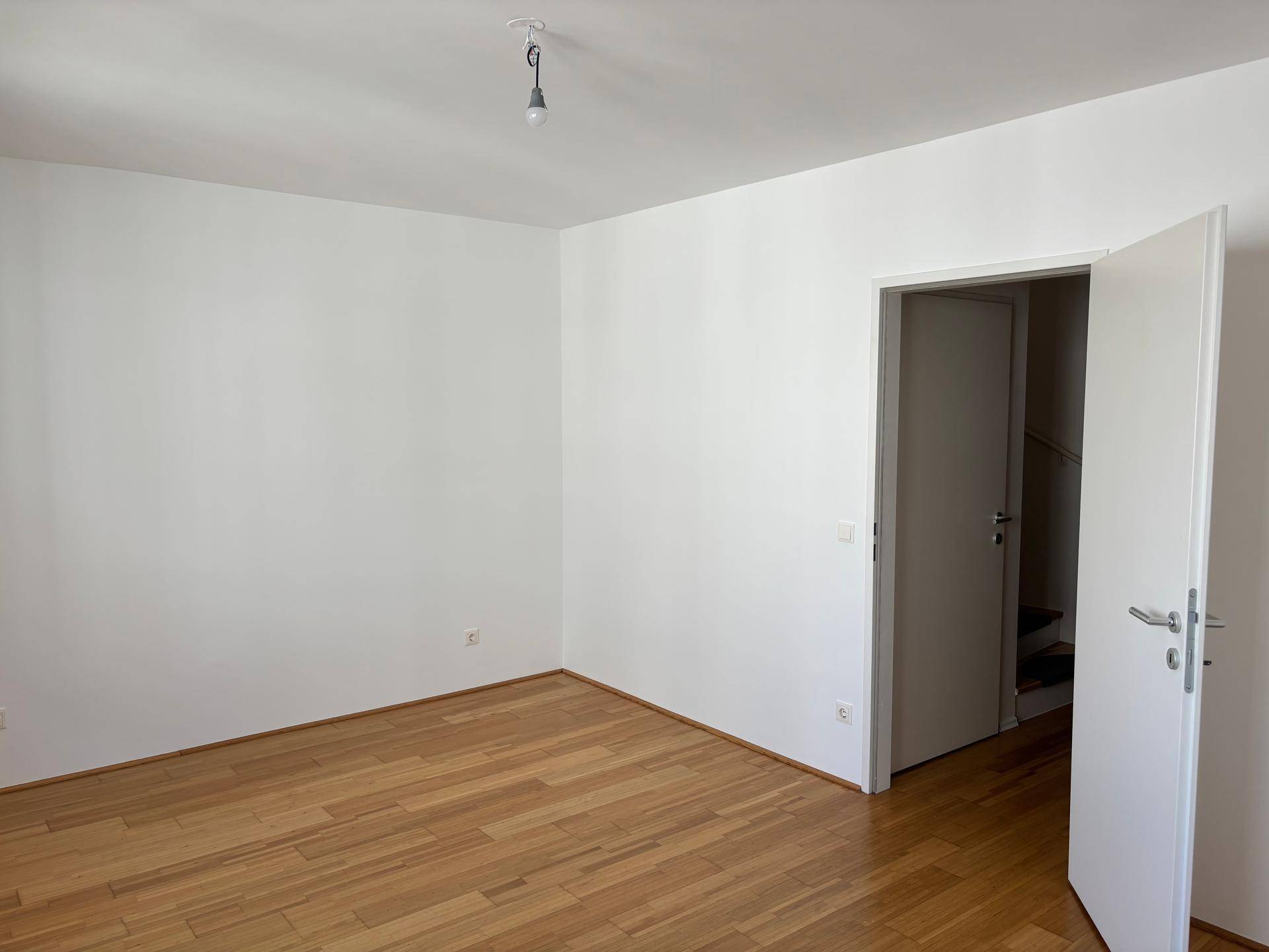 Schlafzimmer mit Parkettboden und offener Tür zum Treppenhaus.