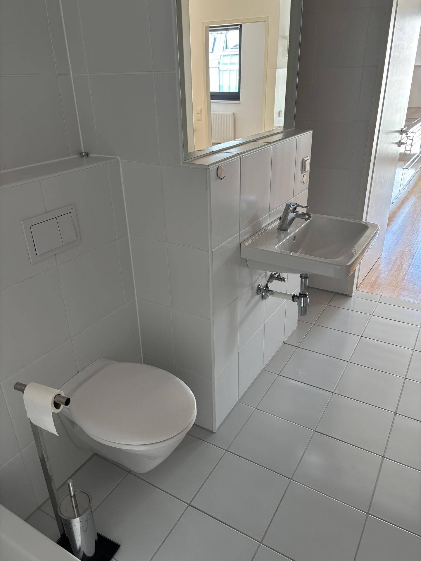 Kleines Gäste-WC mit weiß gefliesten Wänden, wandhängendem WC und Waschbecken.