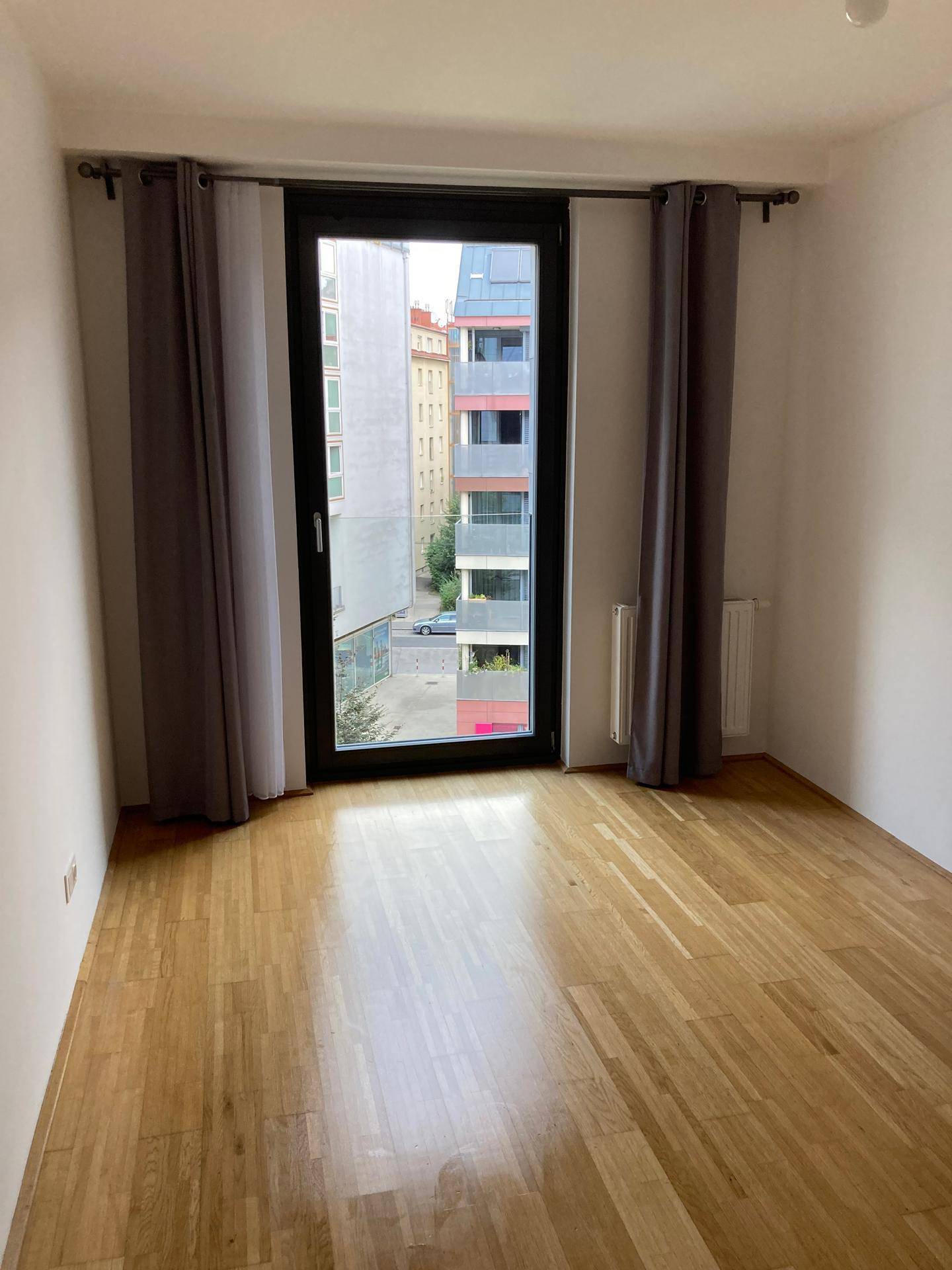 Helles Zimmer mit Parkettboden und großem Fenster, das viel Tageslicht bietet.