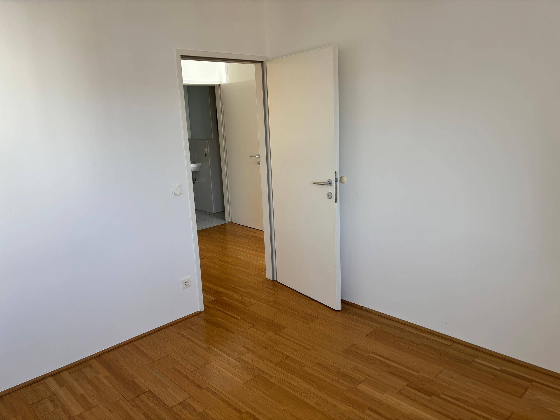 Schlafzimmer mit Parkettboden und offener Tür zu einem angrenzenden Badezimmer.