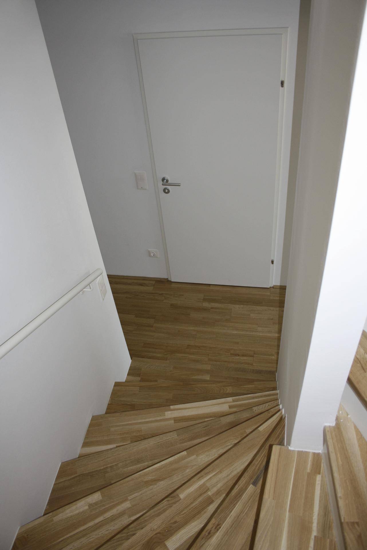 Treppenhaus mit Holzstufen und weiß gestrichenen Wänden, das die Etagen verbindet.