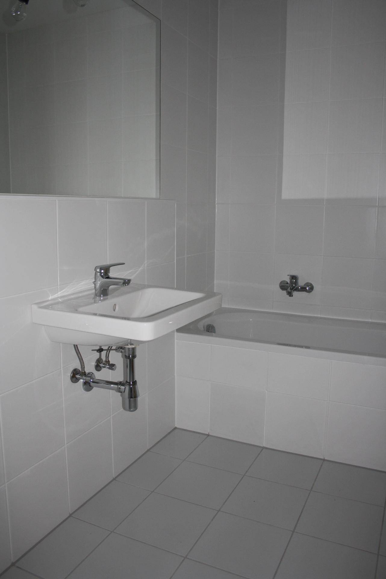 Badezimmer mit weißen Fliesen, Waschbecken und integrierter Badewanne.