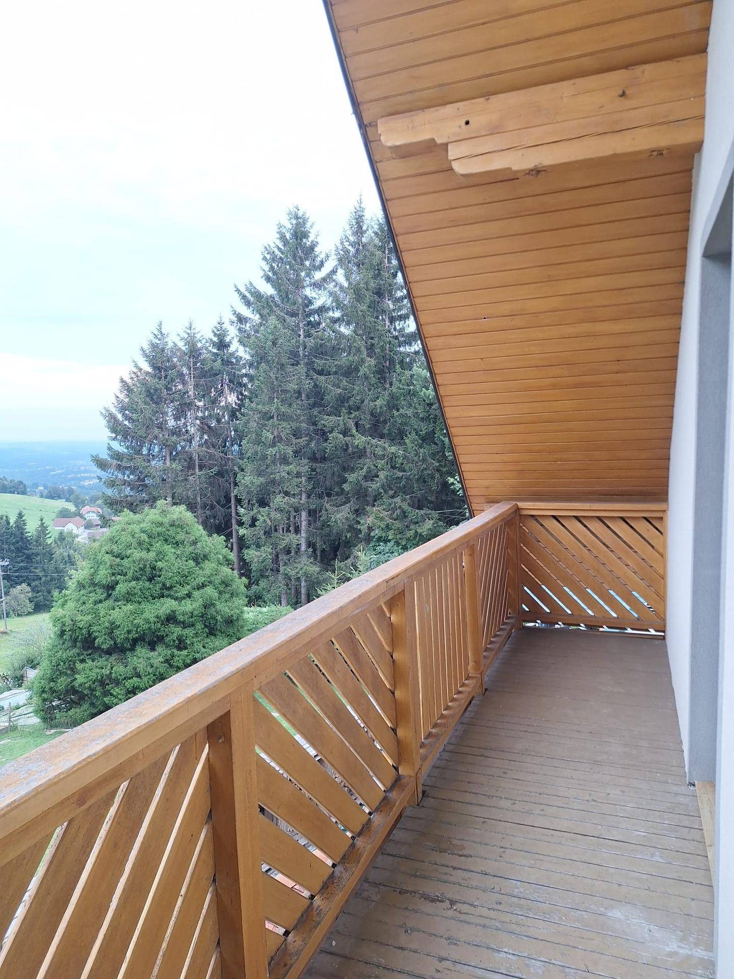 Holzbalkon mit Geländer und weitem Blick über bewaldete Hügel und die umliegende Landschaft.