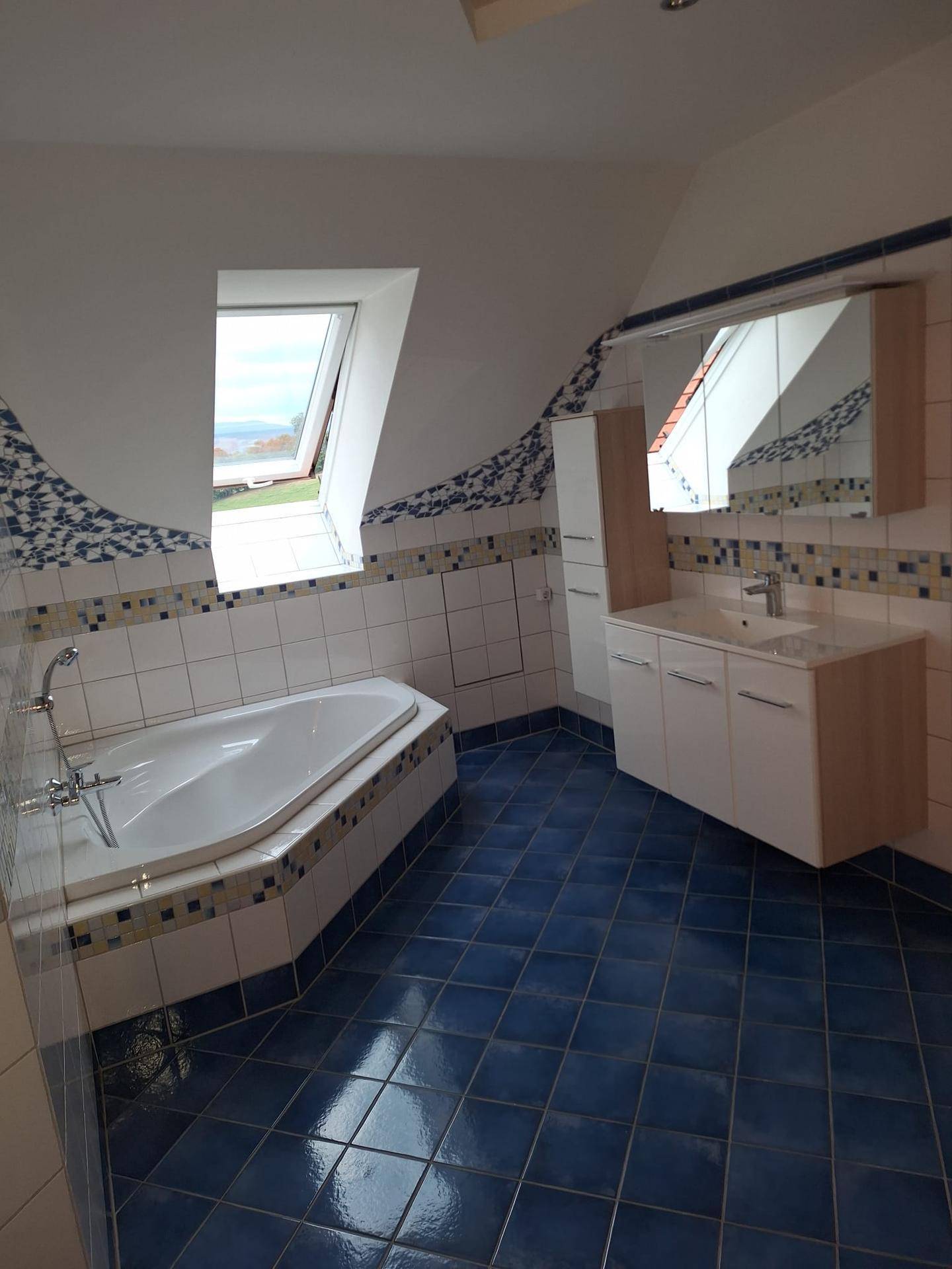 Geräumiges Badezimmer mit Eckbadewanne, Doppelwaschbecken und Dachfenster, blau gefliest.
