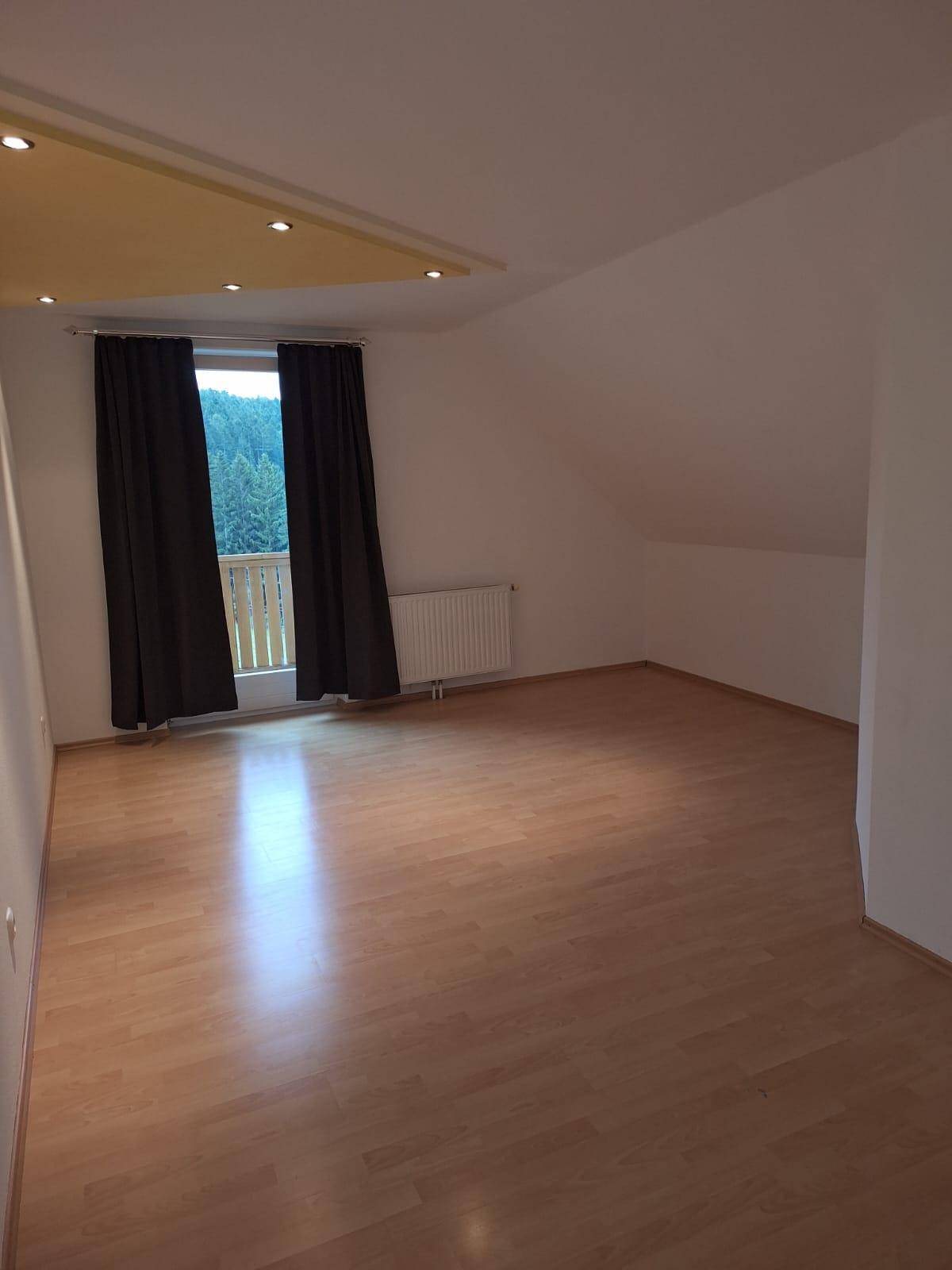 Helles Schlafzimmer mit Laminatboden, Dachschrägen und Zugang zu einem kleinen Balkon.