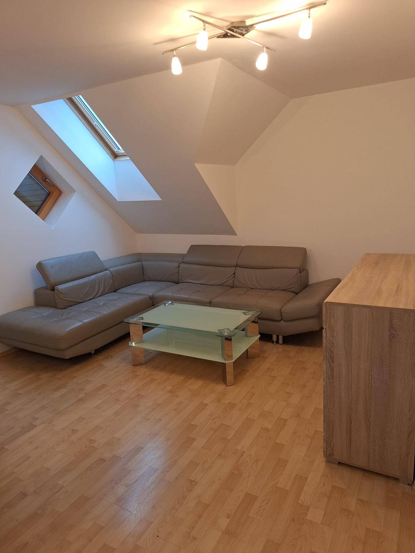 Wohnzimmer im Dachgeschoss mit Schrägdach, Dachfenstern und beiger Eckcouch auf Laminatboden.