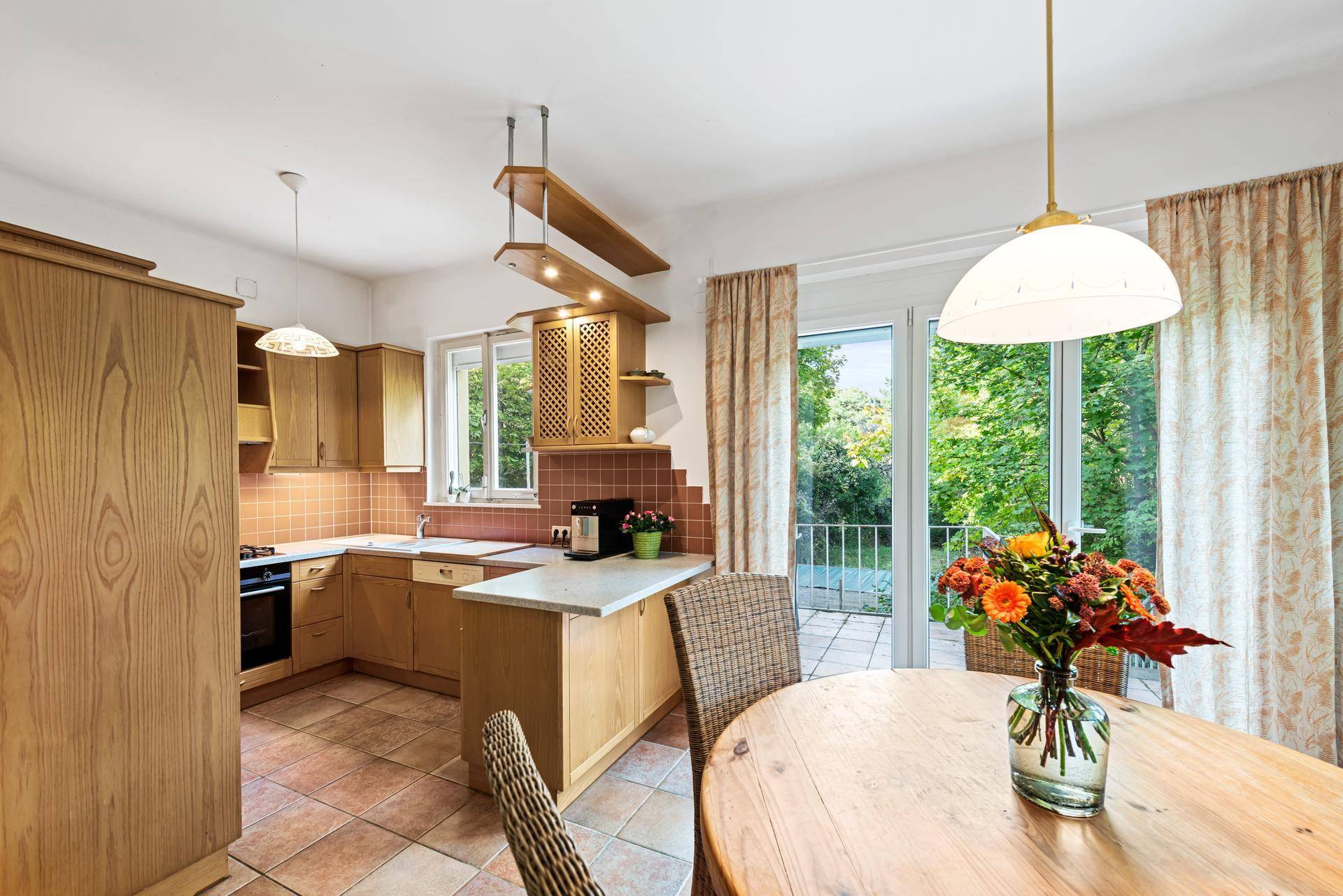 Küche mit Holzeinbauten, Essbereich und Zugang zur Terrasse mit Gartenblick.
