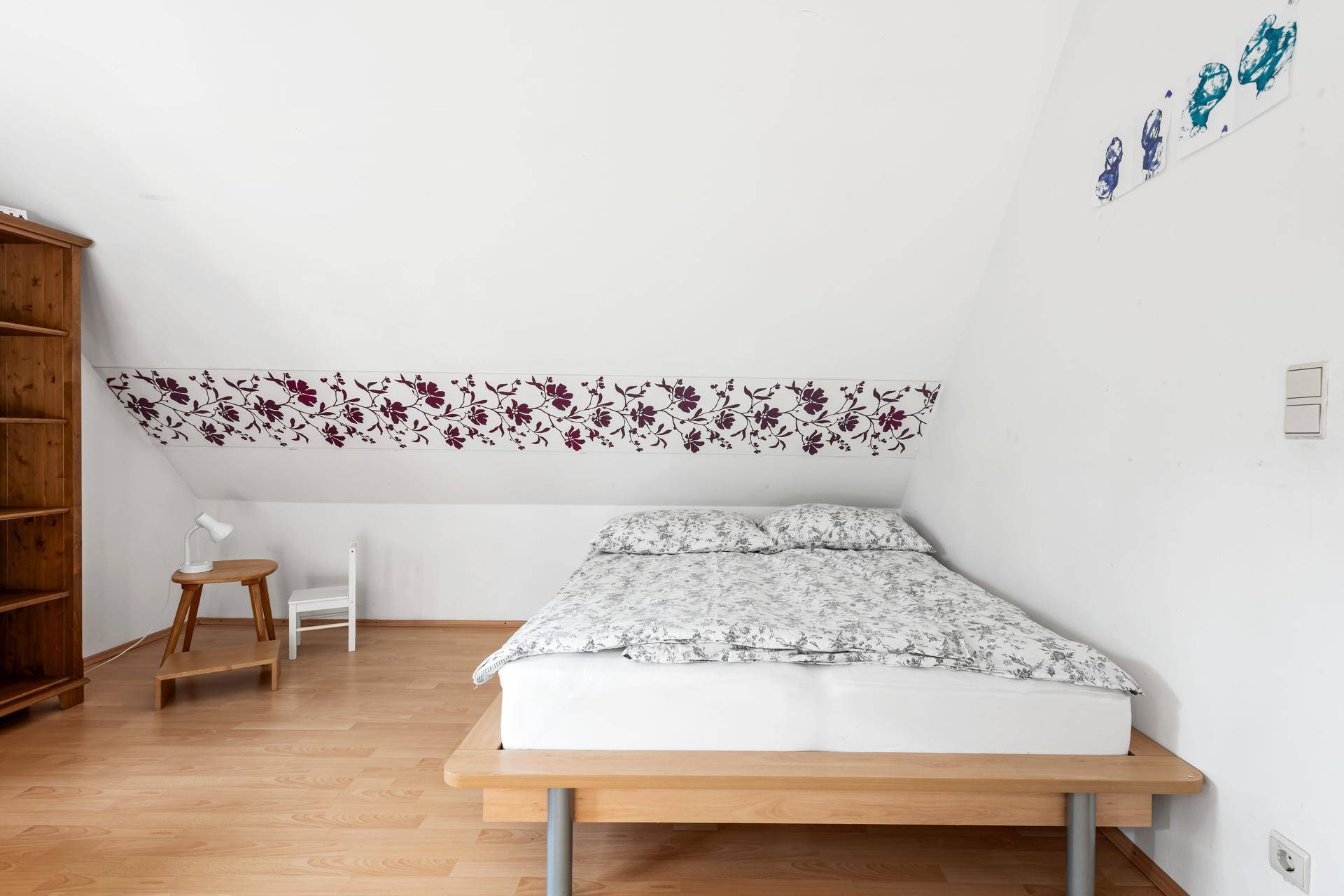 Schlafzimmer im Dachgeschoss mit Holzboden und floraler Wanddekoration.