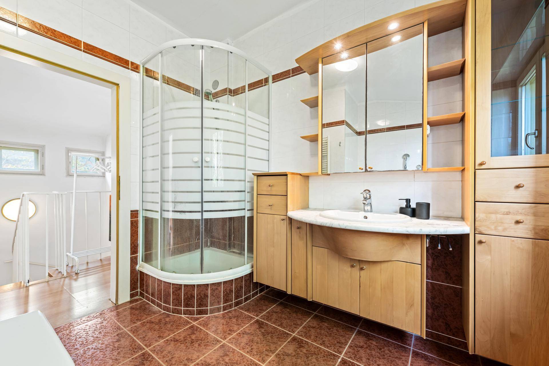 Badezimmer mit Duschkabine, Holzwaschtisch und braunen Bodenfliesen.