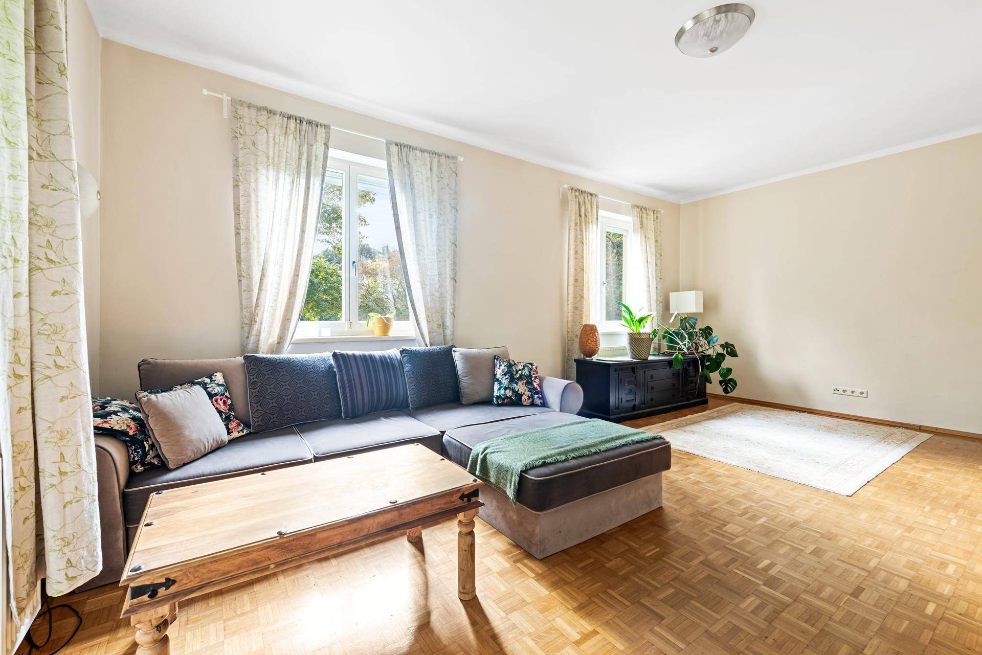 Helles Wohnzimmer mit beigem Sofa, Holzboden und Blick in den grünen Garten.