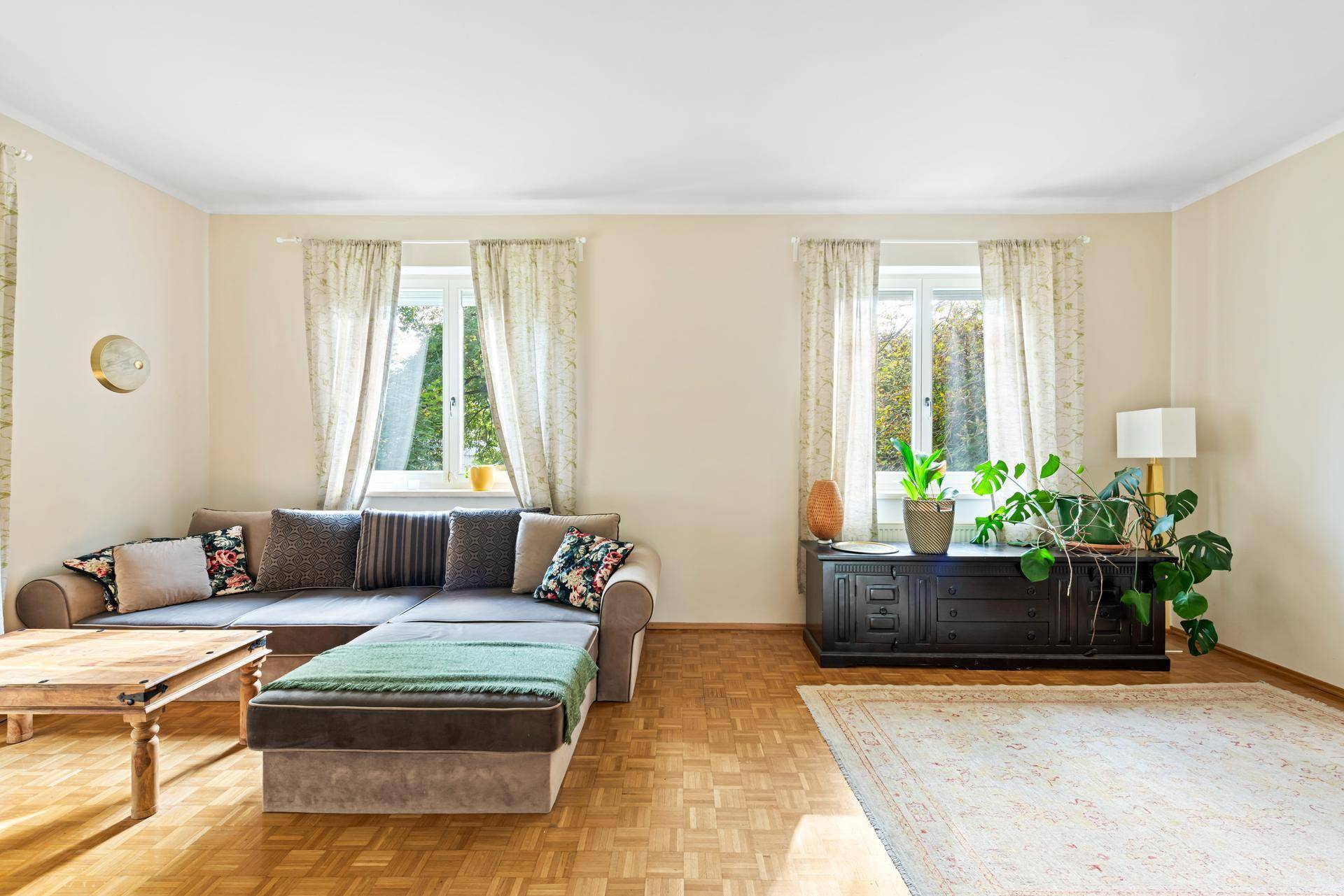 Geräumiges Wohnzimmer mit Holzboden, beigen Wänden und viel Tageslicht.