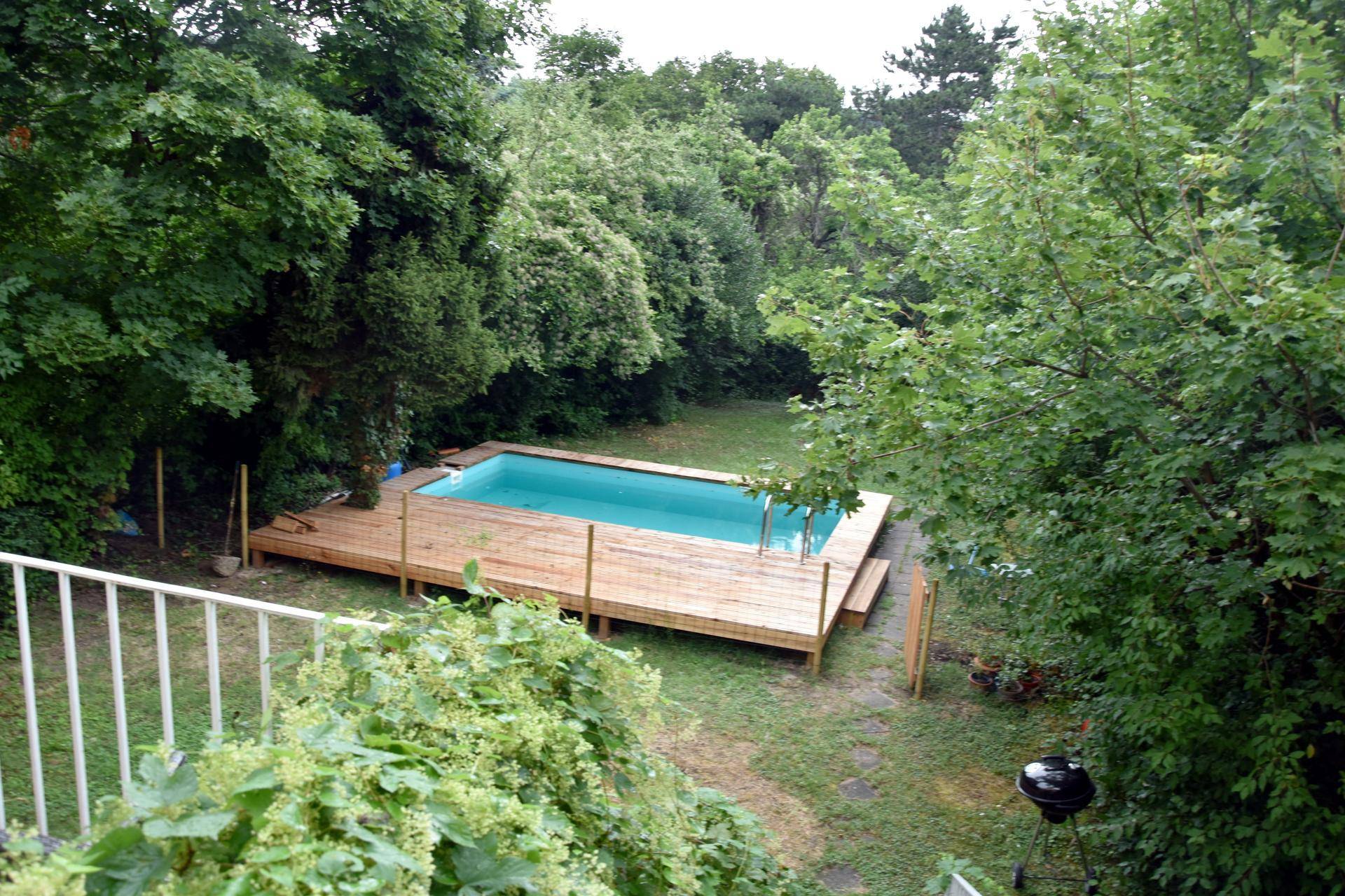 Großer Garten mit Swimmingpool und Holzdeck, umgeben von Bäumen und Sträuchern.