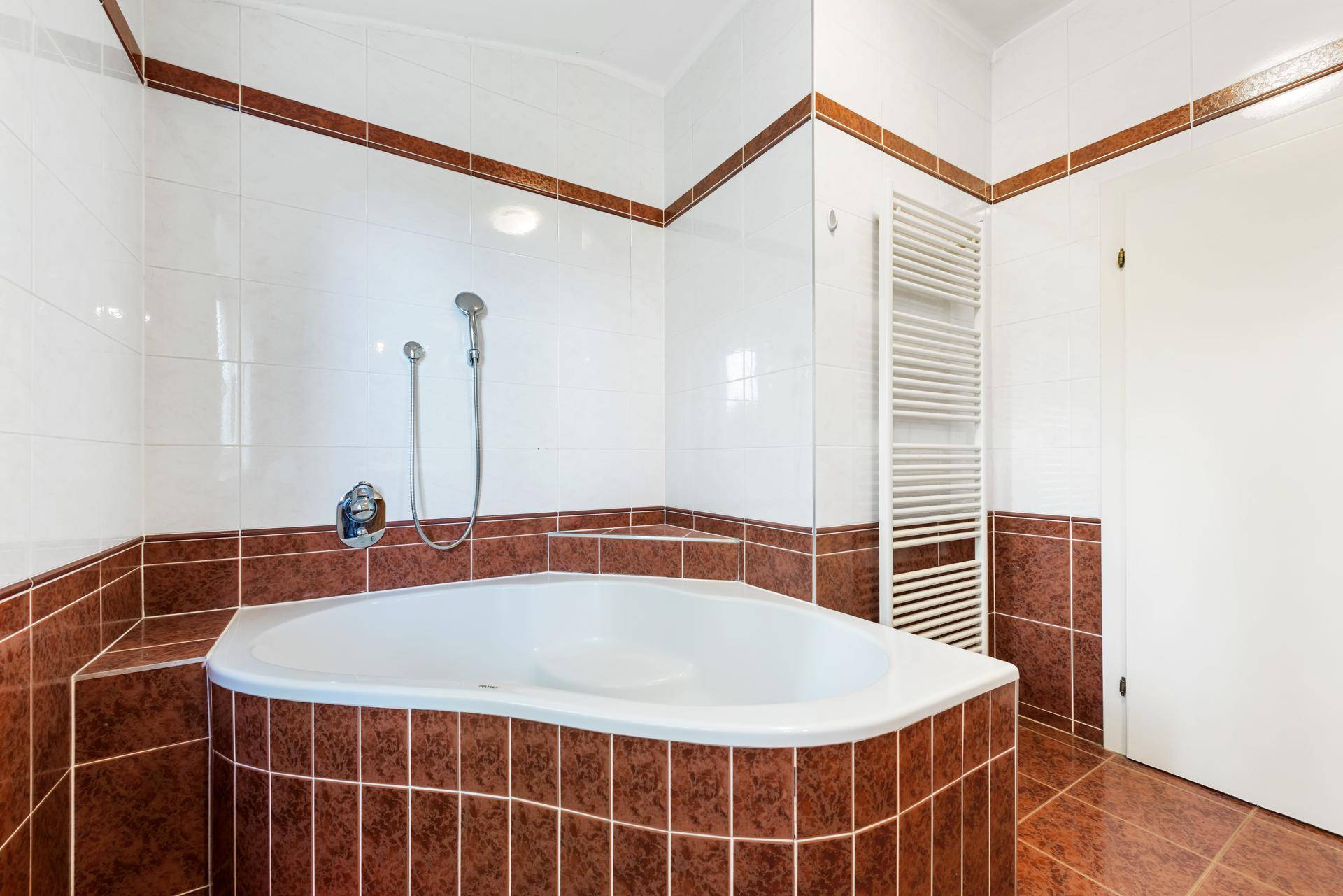 Badezimmer mit Eckbadewanne, braunen Fliesen und weißer Wandgestaltung.