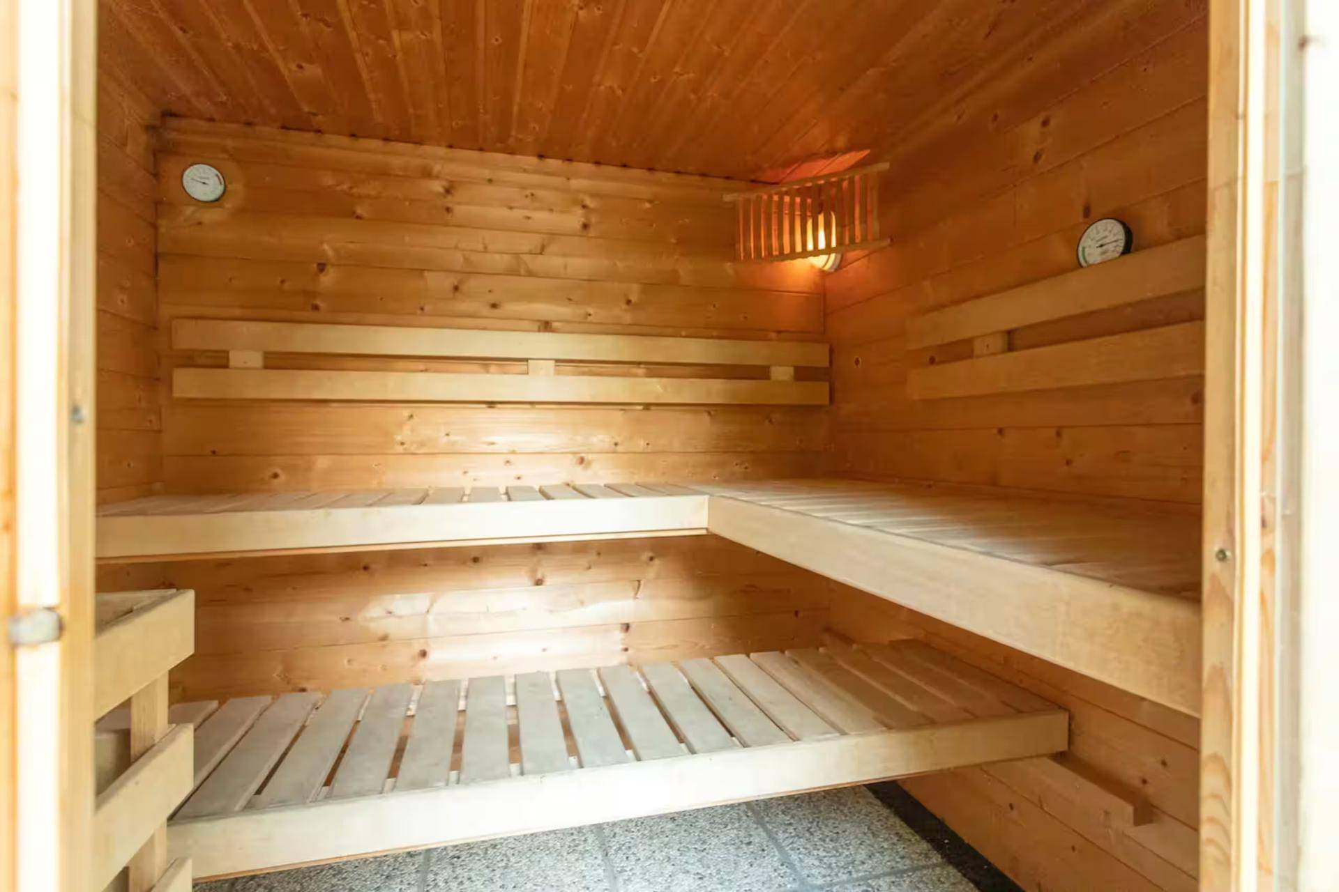 Holzvertäfelte Sauna mit Sitzbänken und Temperaturanzeige für Entspannung.