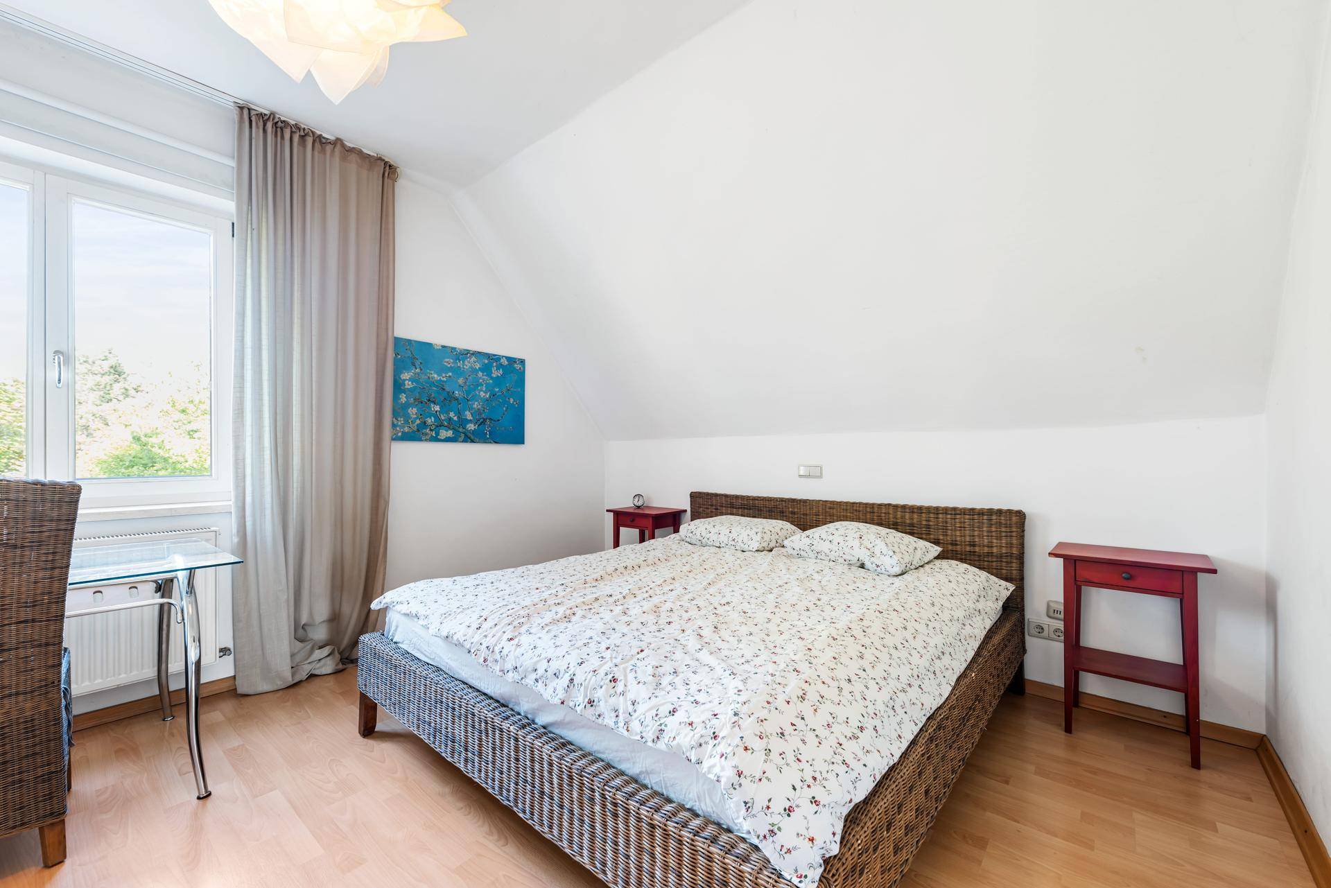 Schlafzimmer im Dachgeschoss mit schrägen Wänden, Rattanbett und Holzboden.