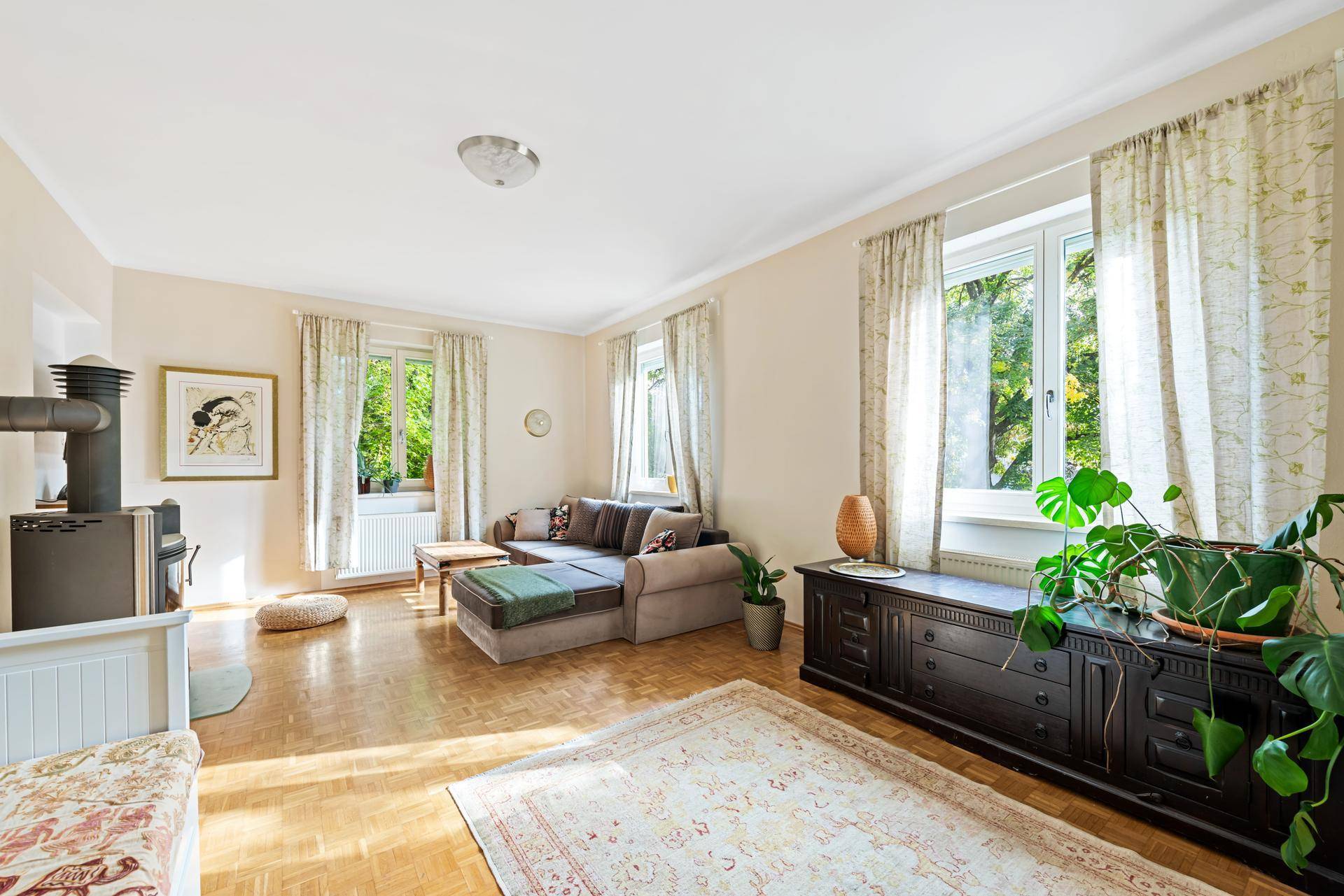 Gemütliches Wohnzimmer mit Holzboden, Kaminofen und großen Fenstern zum Garten.