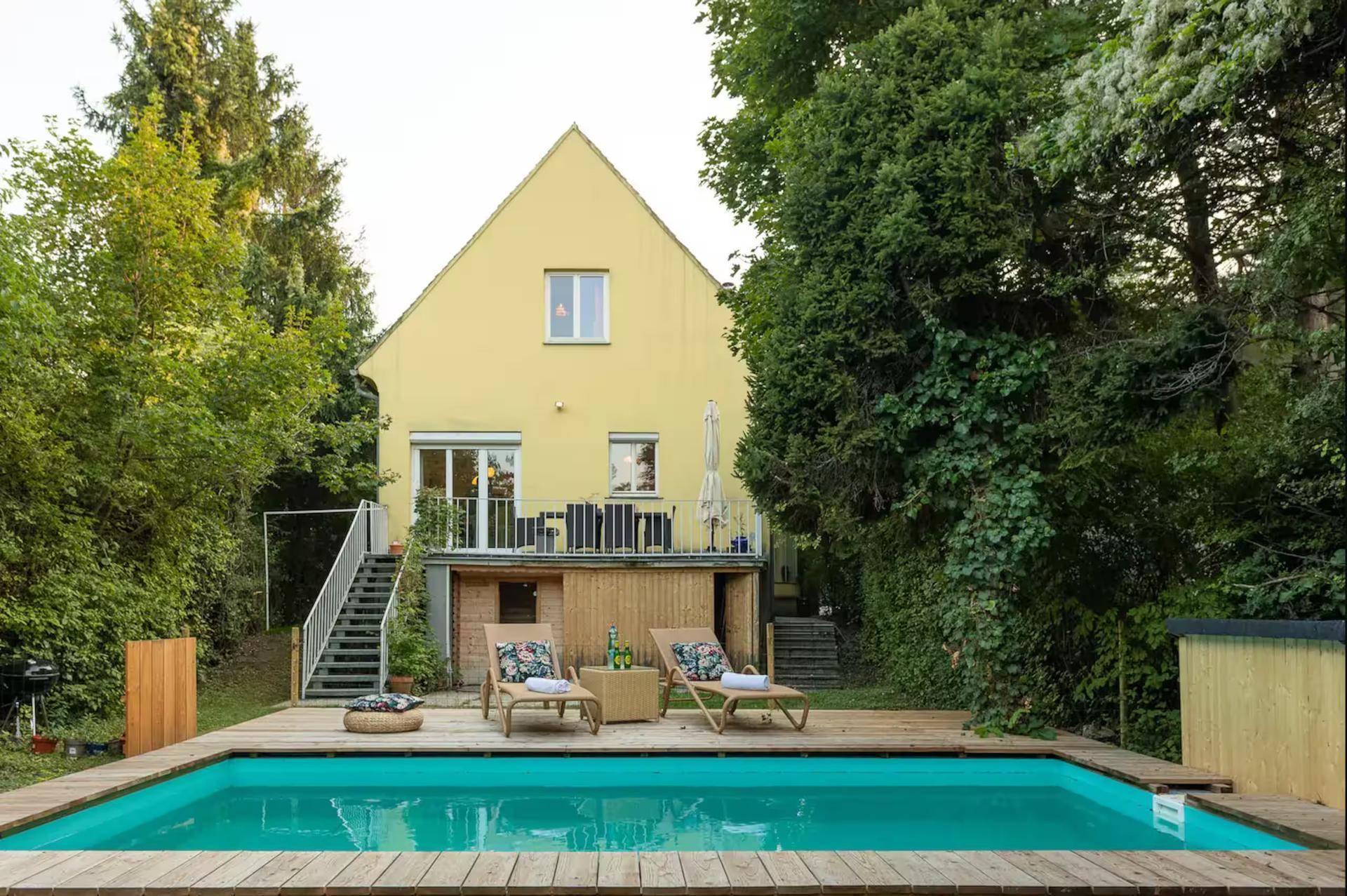 Gelbes Haus mit Garten, Terrasse und Swimmingpool umgeben von viel Grün.
