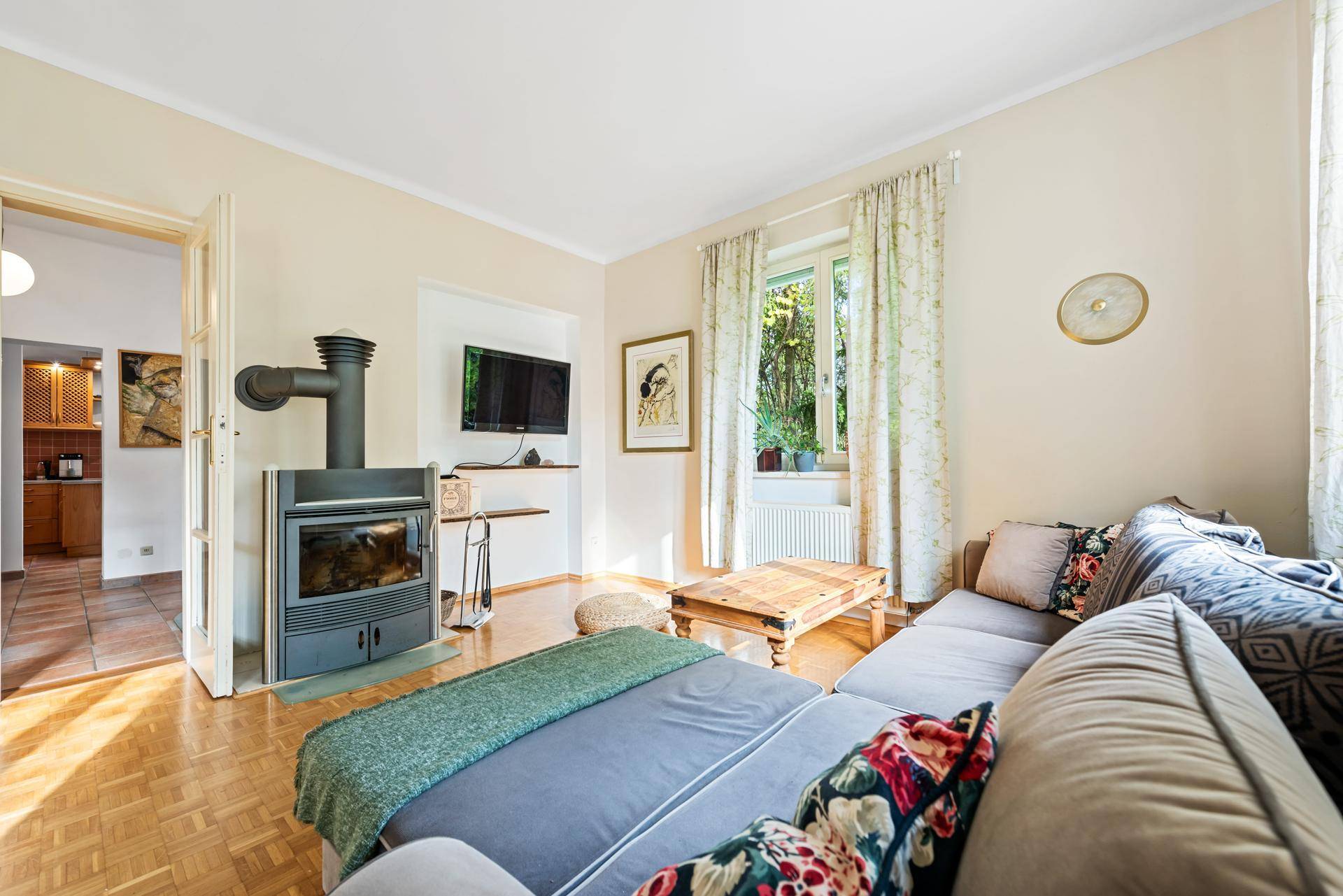 Wohnzimmer mit Kaminofen, Holzboden und Blick in die angrenzende Küche.