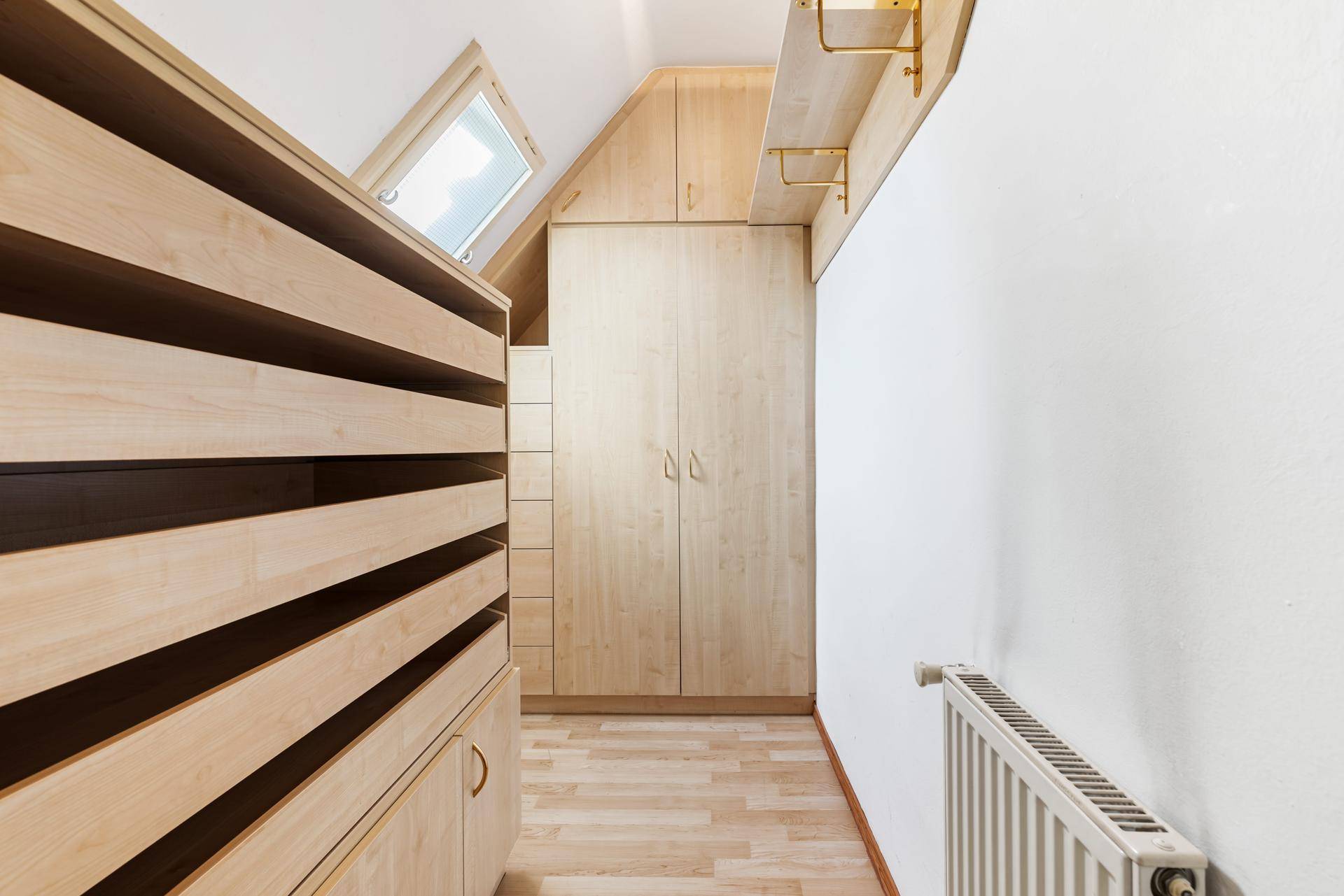 Begehbarer Kleiderschrank mit maßgefertigten Holzschränken und Dachfenster.