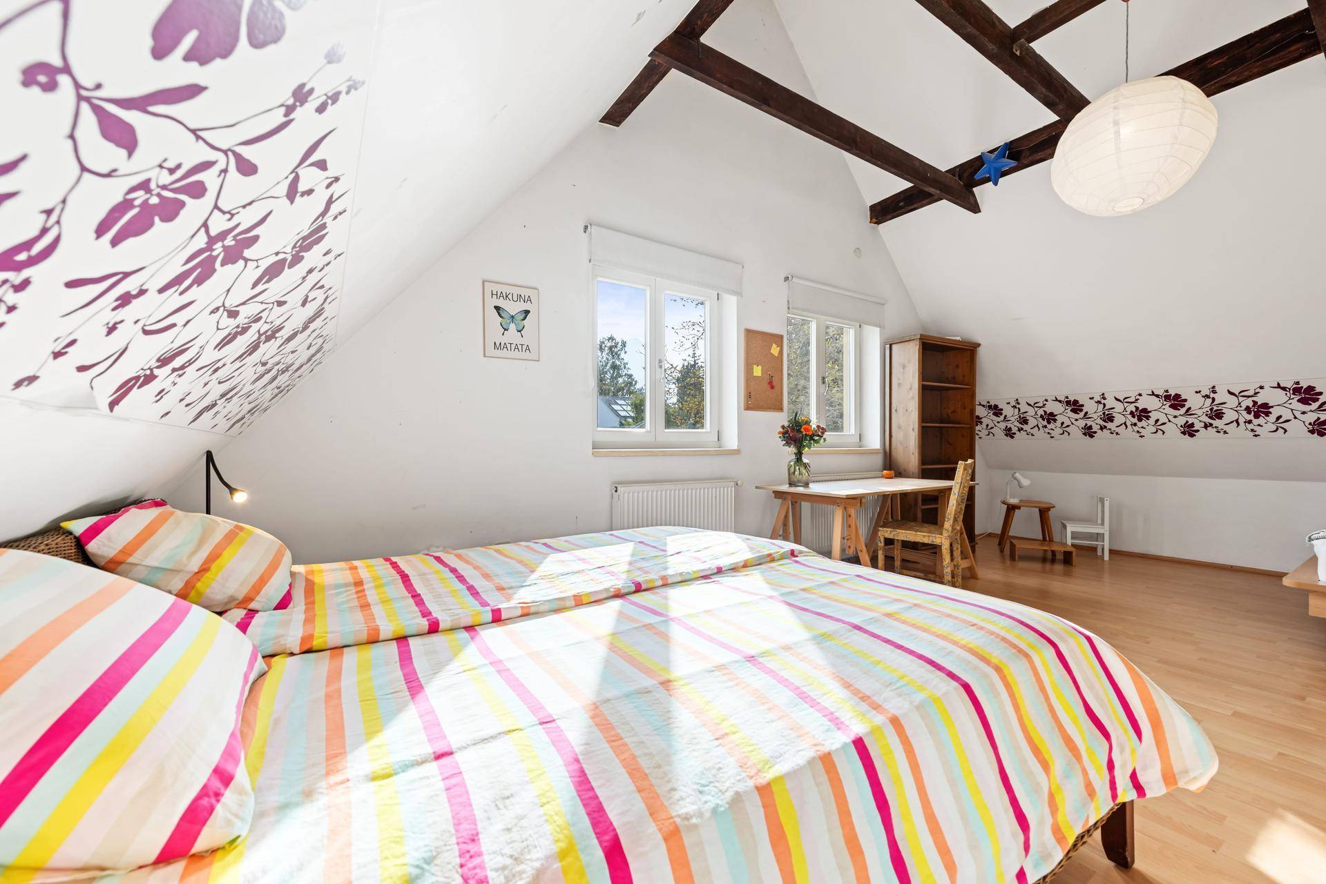 Helles Schlafzimmer im Dachgeschoss mit farbenfroher Bettwäsche und Holzboden.