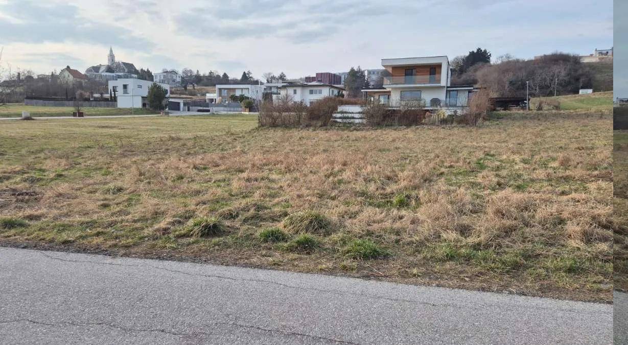 Blick über ein trockenes Feld auf moderne Häuser und eine Kirche in der Ferne.