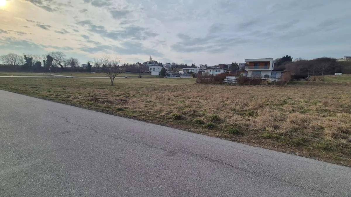 Weitläufiges Feld mit Straße im Vordergrund und Häusern sowie Kirche im Hintergrund.