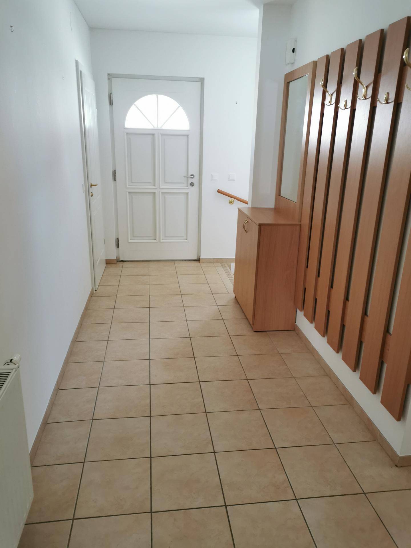 Heller Eingangsbereich mit Fliesenboden, Garderobe und weißer Haustür mit Glaseinsatz.