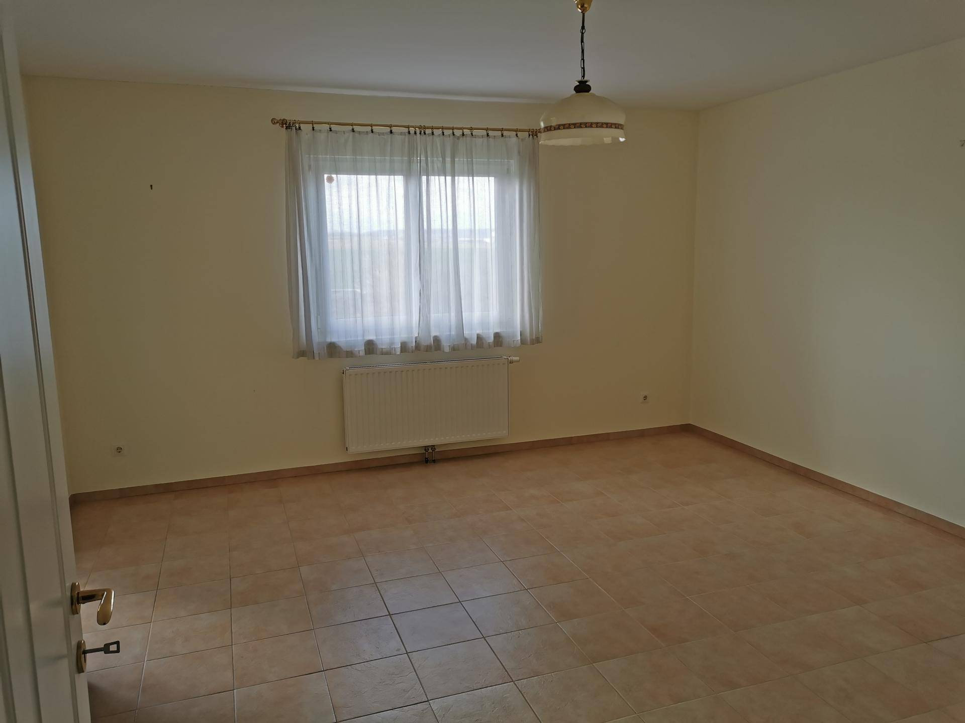 Geräumiges Schlafzimmer mit Fliesenboden, großem Fenster und Heizkörper.
