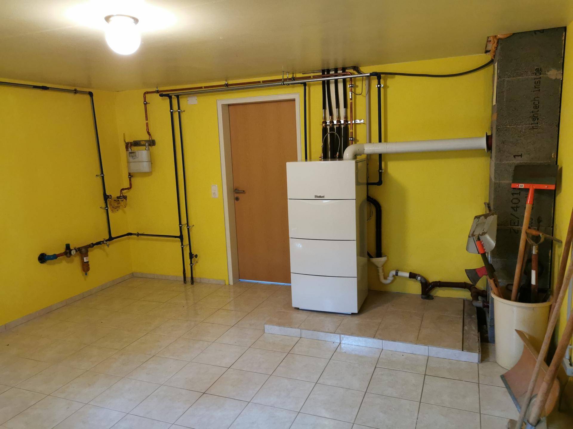 Funktionaler Heizungsraum im Keller mit gelben Wänden, Fliesenboden und sichtbaren Installationen.
