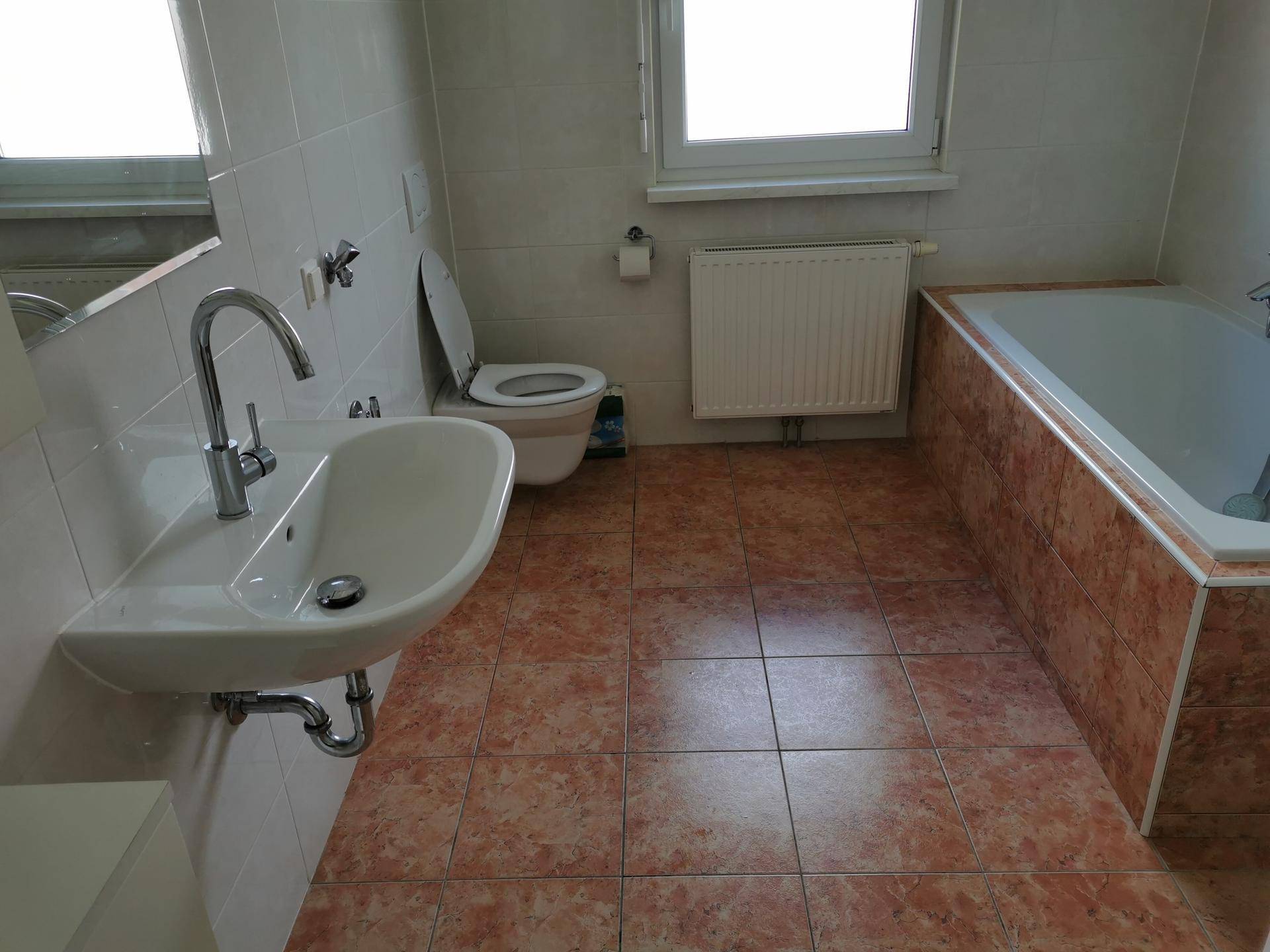 Geräumiges Badezimmer mit Waschbecken, Badewanne, Wand-WC und terracottafarbenen Fliesen.