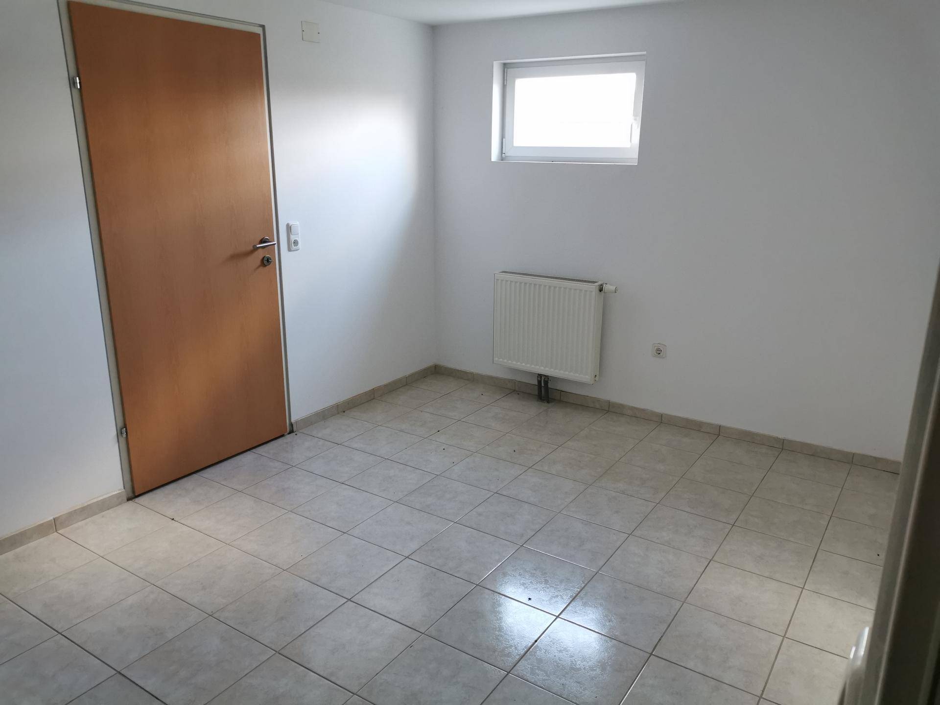 Raum im Untergeschoss mit Fliesenboden, Fenster und weiß gestrichenen Wänden.