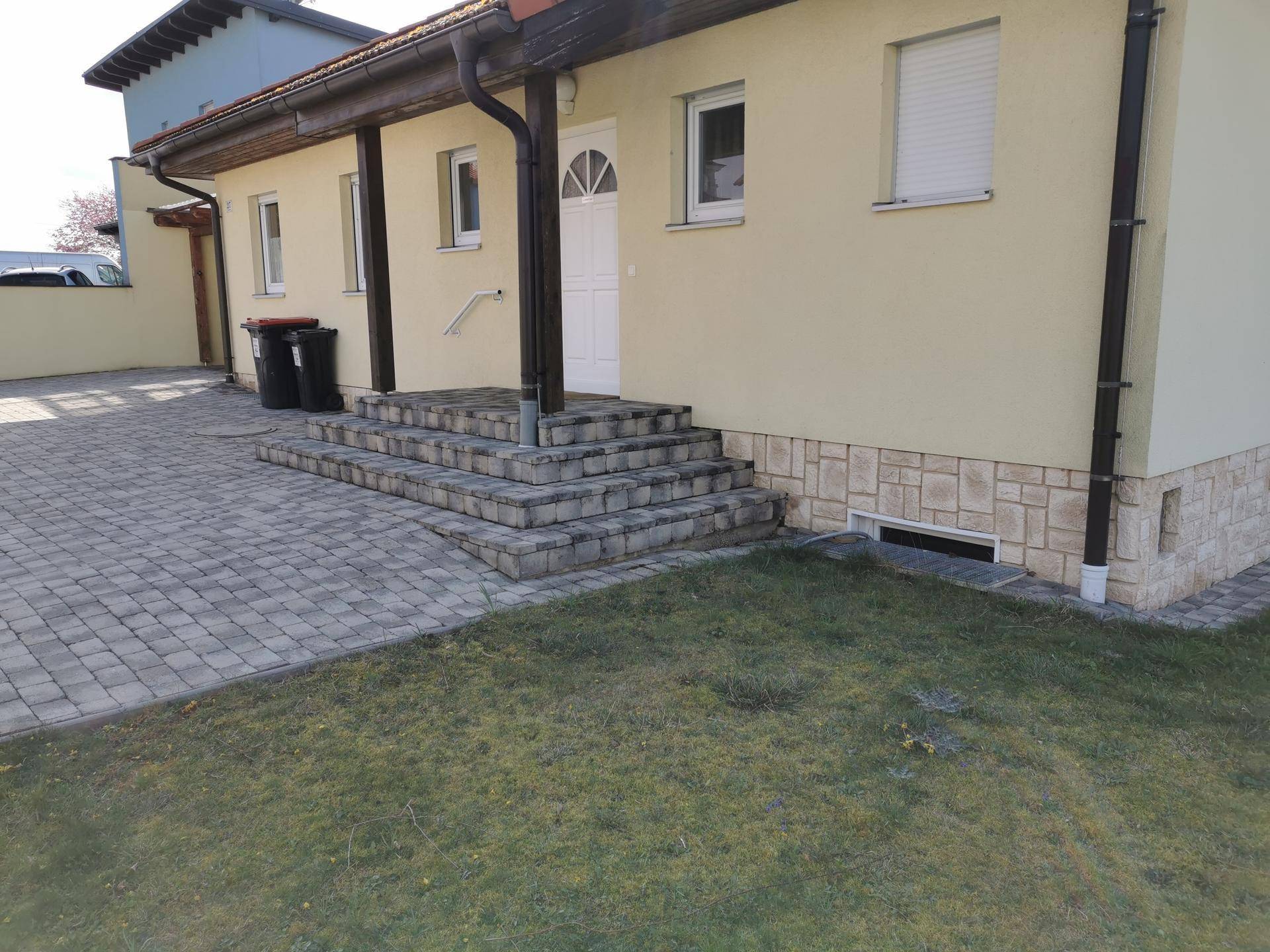 Seitlicher Eingangsbereich des Hauses mit gepflastertem Weg, Treppe und kleinem Rasenstück.