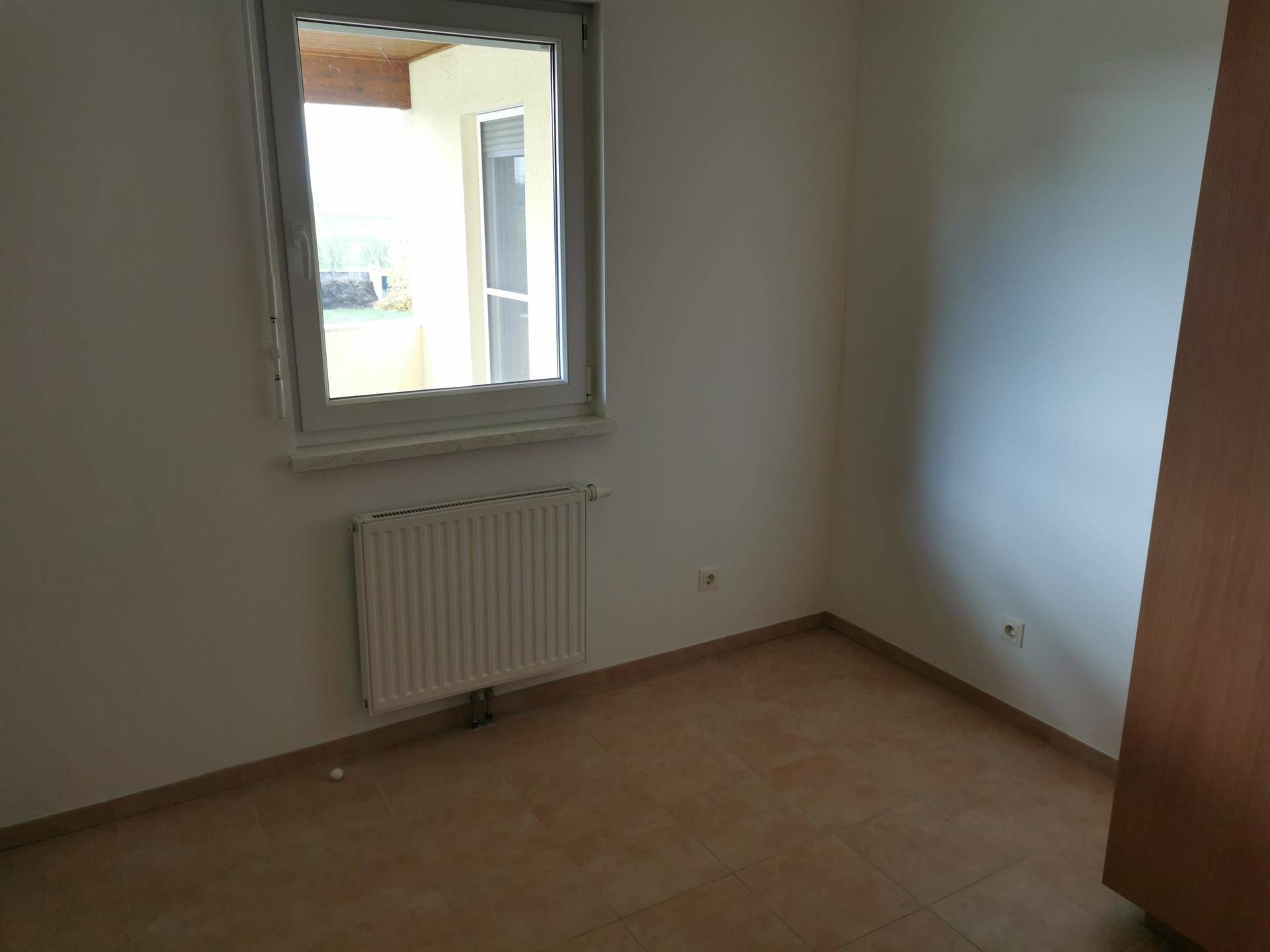 Helles Schlafzimmer mit Fliesenboden und Fenster mit Blick nach draußen.