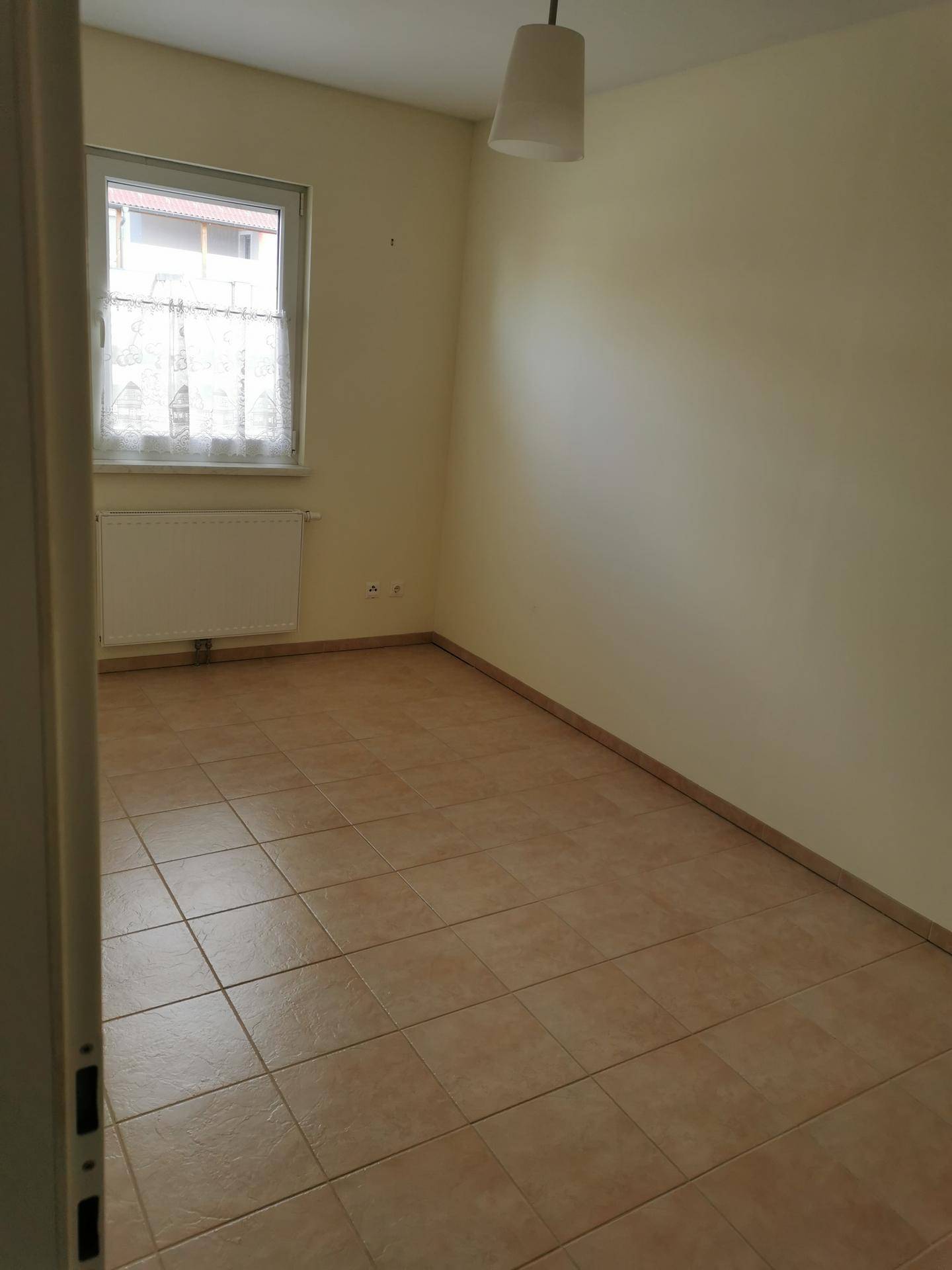 Schlafzimmer mit Fliesenboden und Fenster, das viel Tageslicht hereinlässt.